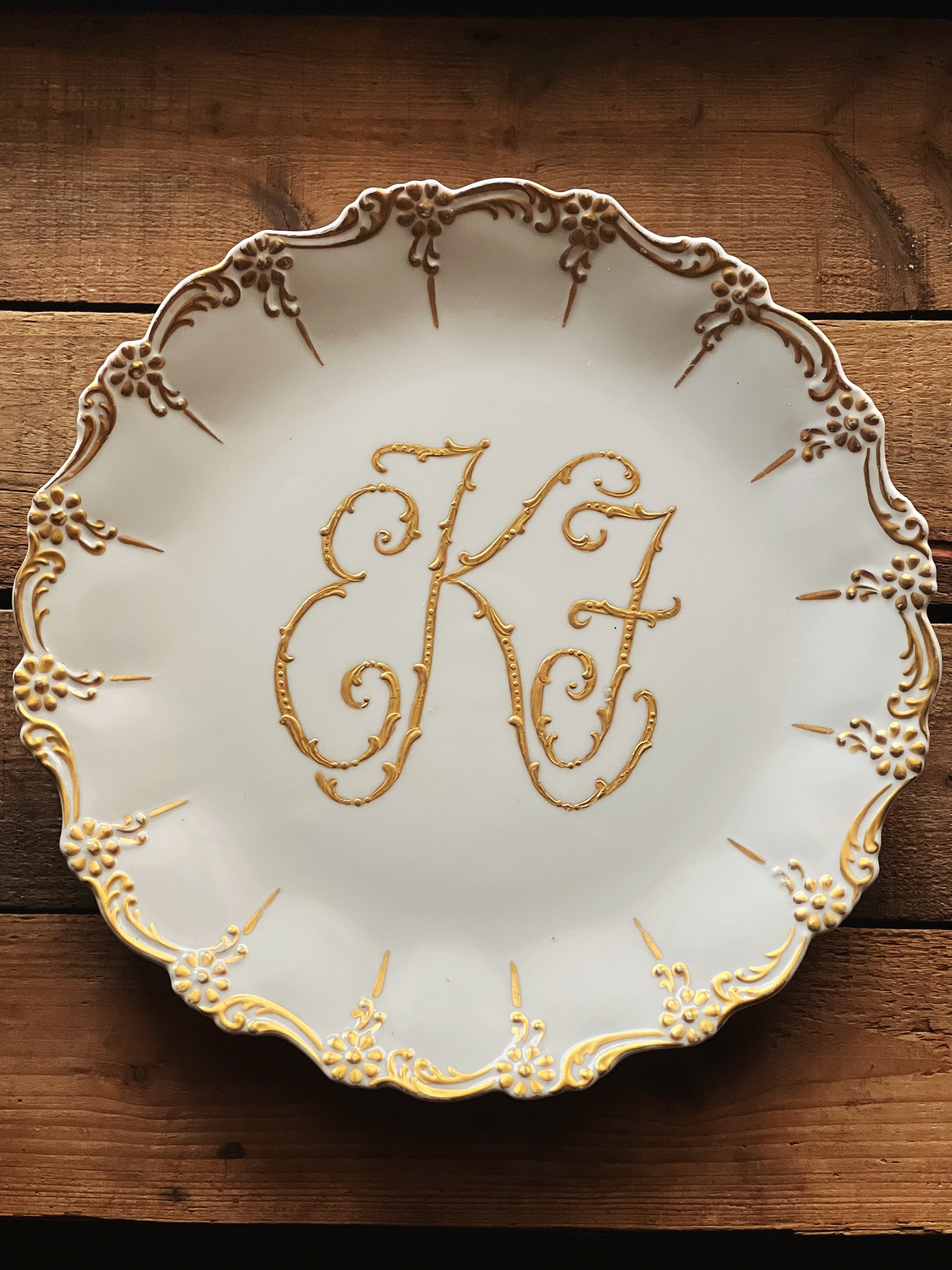 white platter with a gold monogram and elaborate rim design