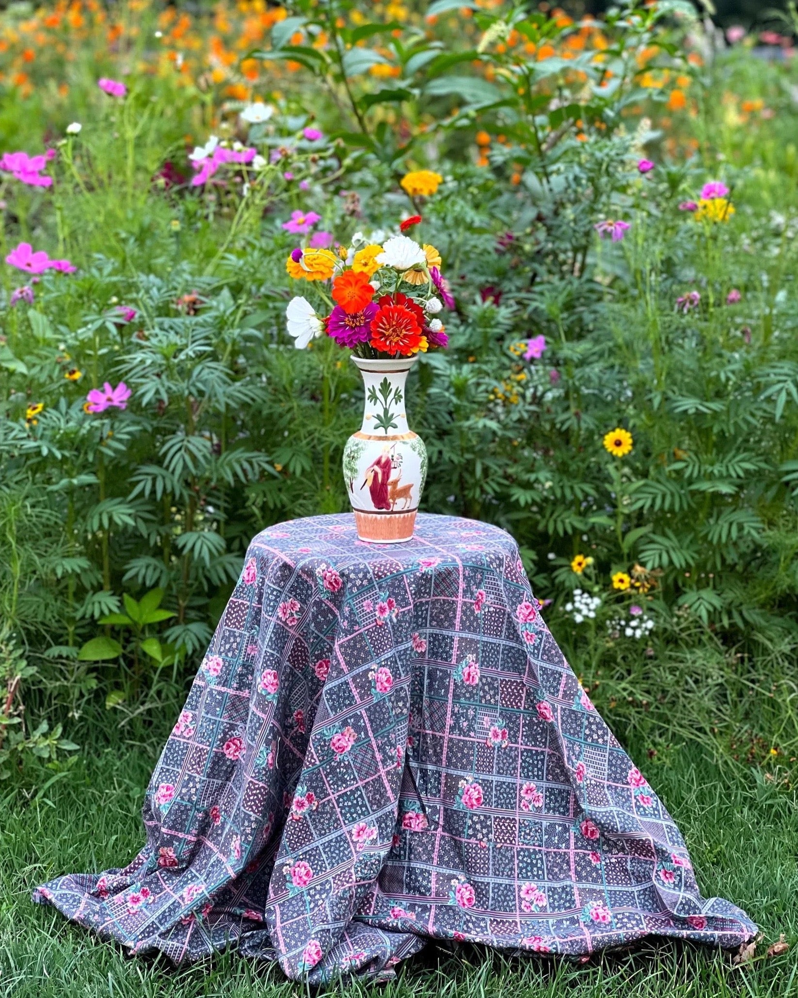 small round table with a floral tablecloth nestled in the middle of a garden