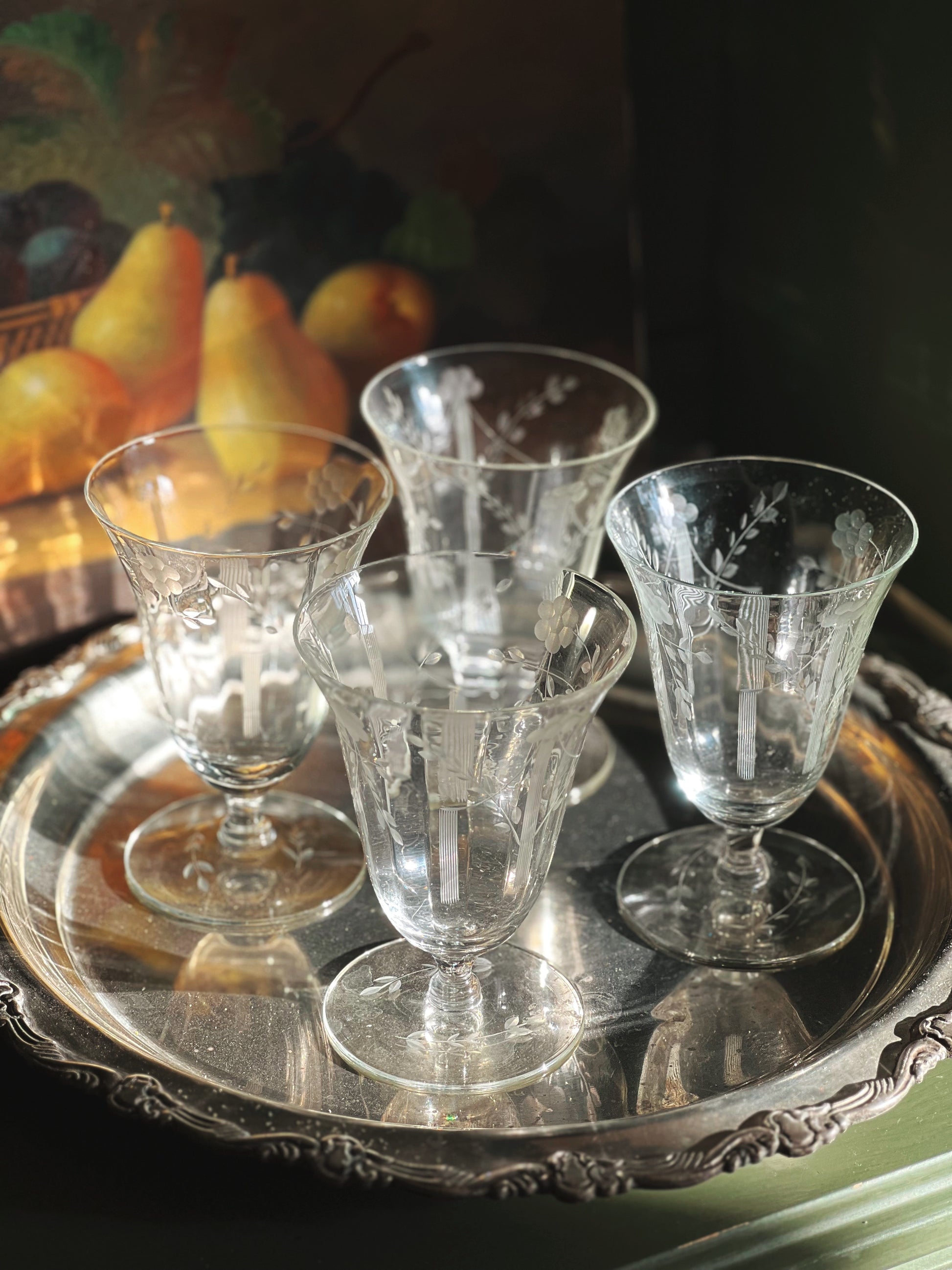 Set of etched glass goblets on a silver tray with a fruit basket in the background