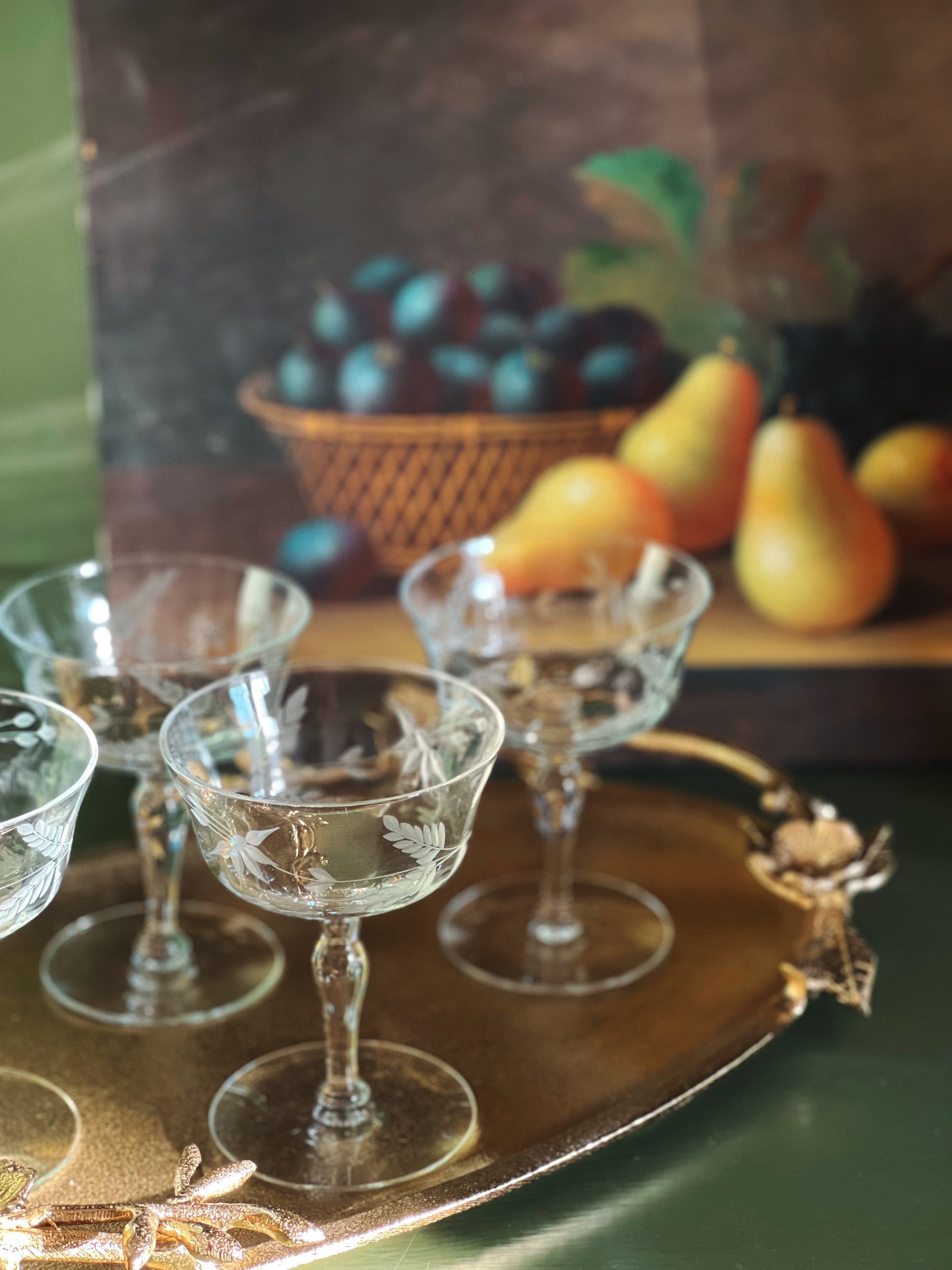 Clear glass goblets on a decorative tray with a blurred background of fruits and a basket.