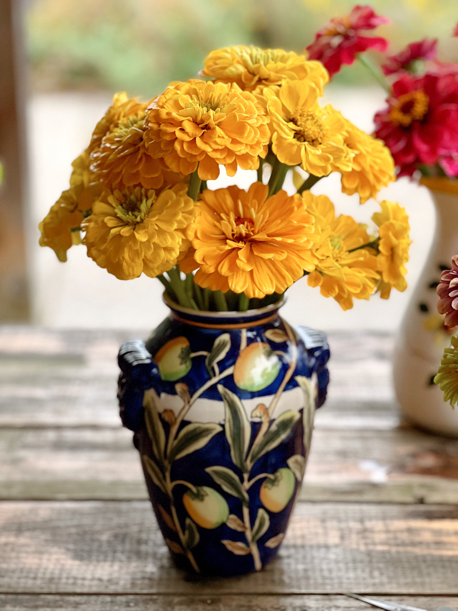 Navy blue vase hand painted with yellow lemons and filled with yellow zinnias