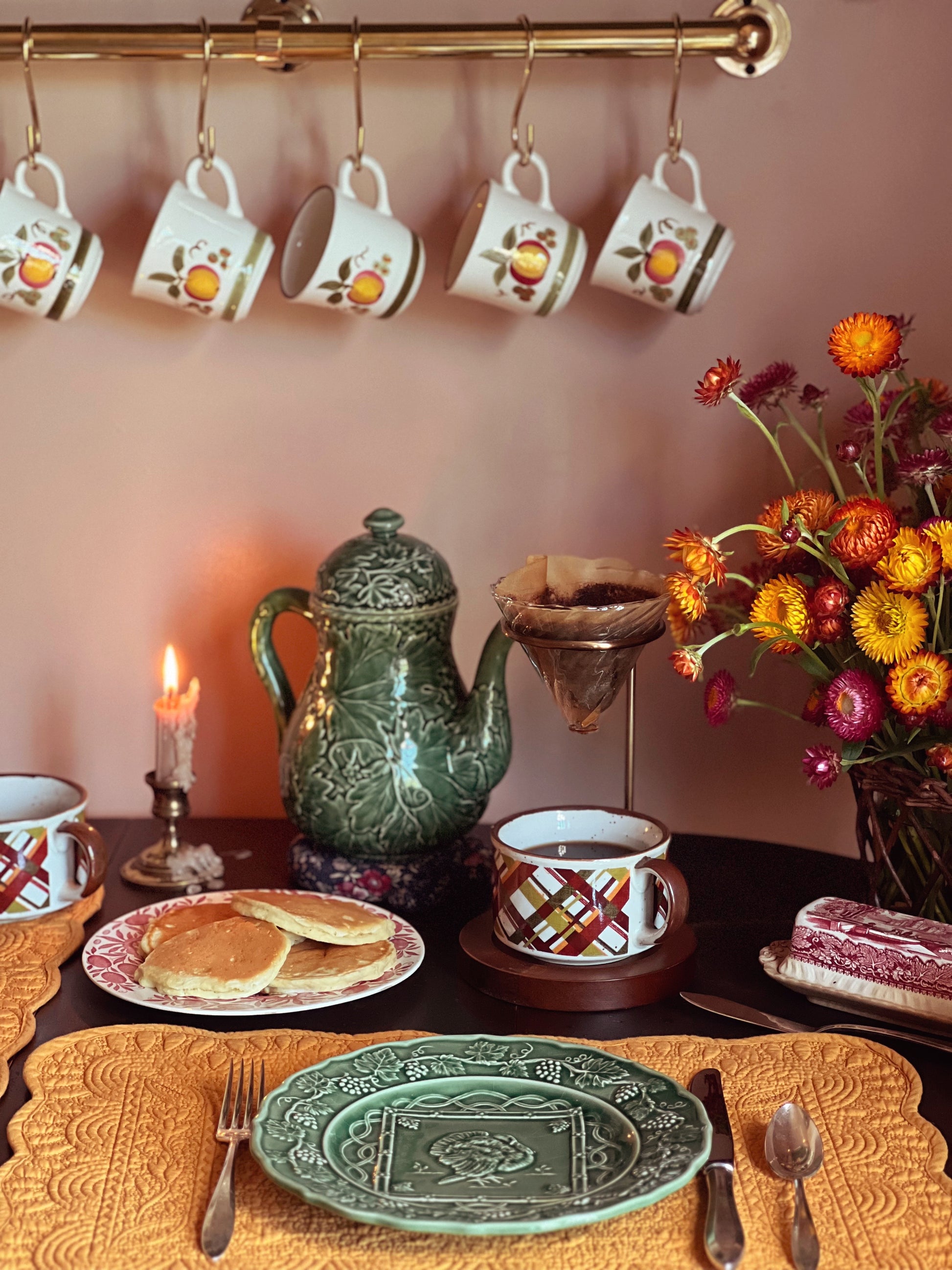 Tea set with teapot, cups, and plates on a table with a candle and flowers.