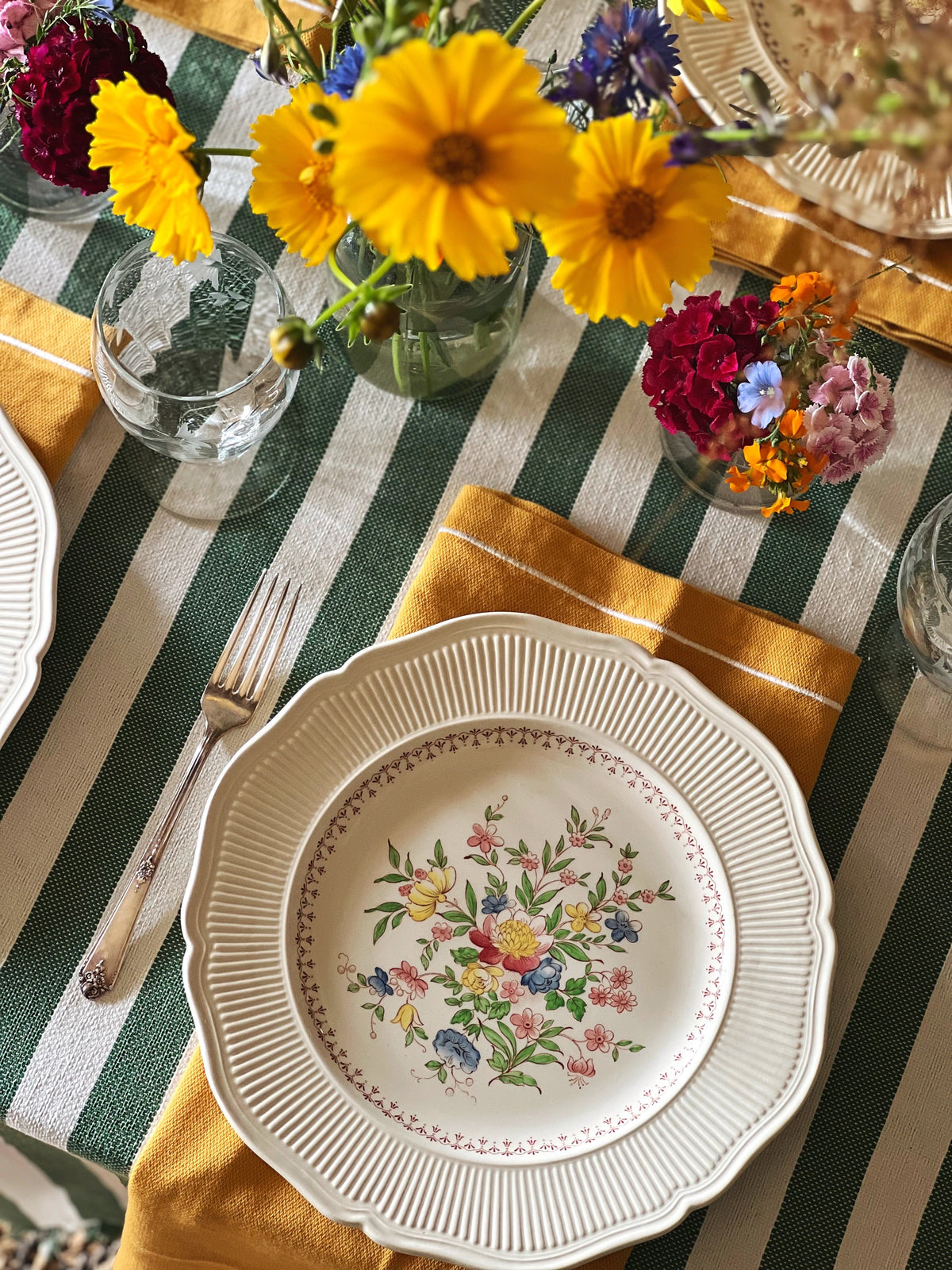 Vintage dinner plates and floral tableware styled on striped linens with colorful summer flowers