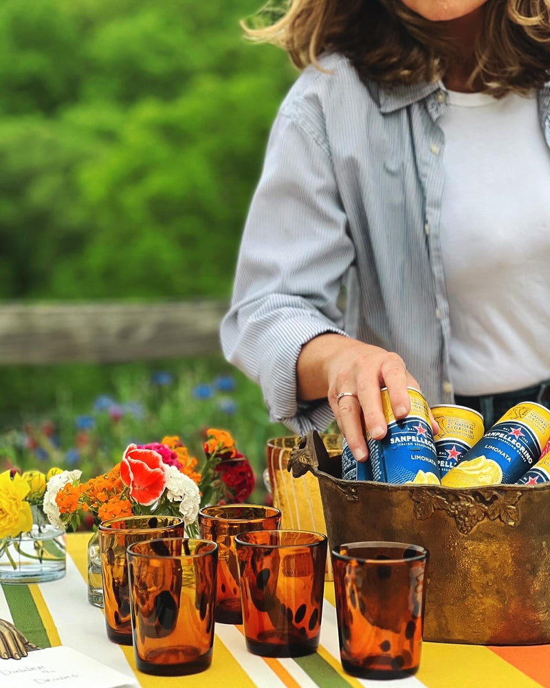 Vintage amber barware and entertaining pieces styled outdoors with striped linens, fresh flowers, and sparkling beverages