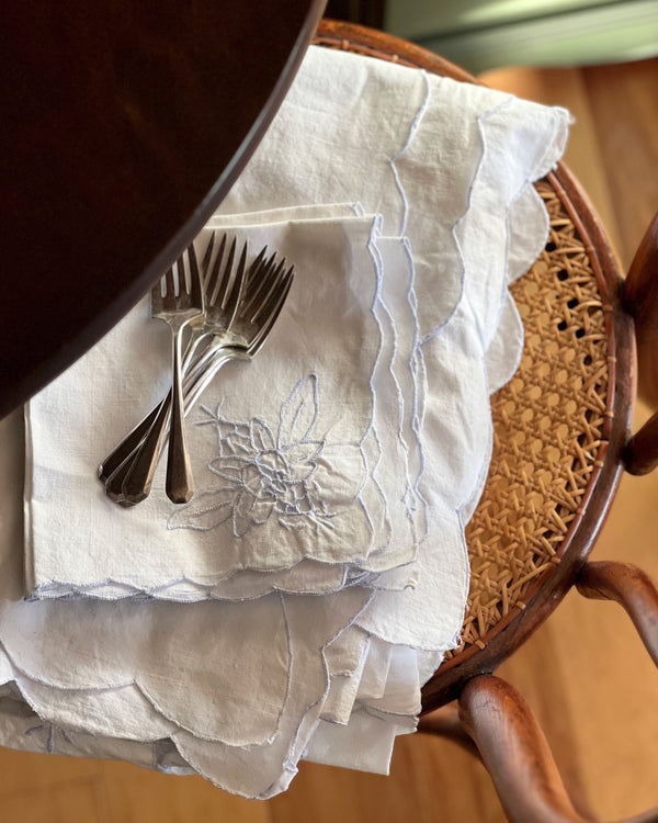 Vintage embroidered table linens draped over a wooden chair with silver flatware and layered gathered textures