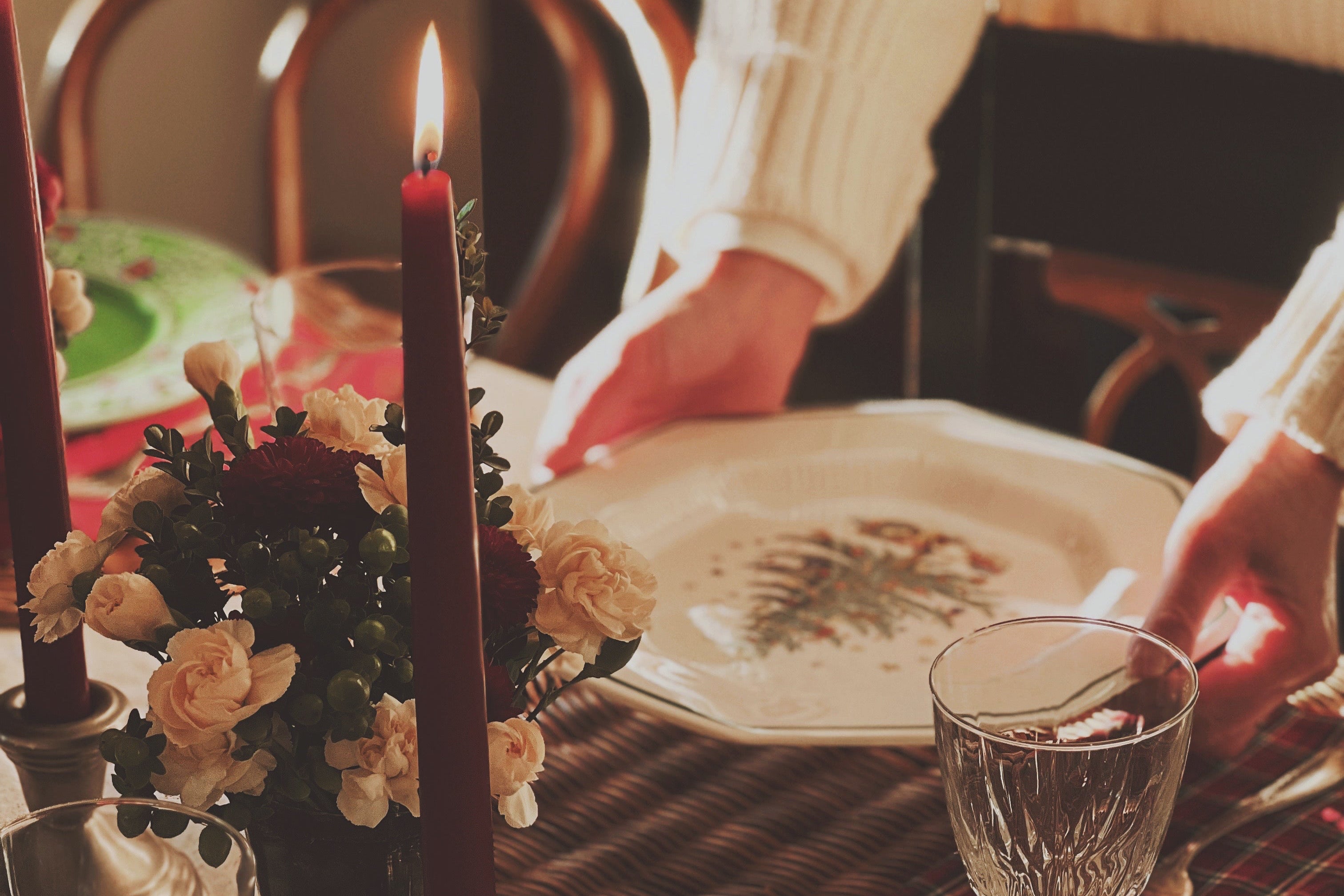 Dining table setting with candles, glasses, and a person holding a plate.