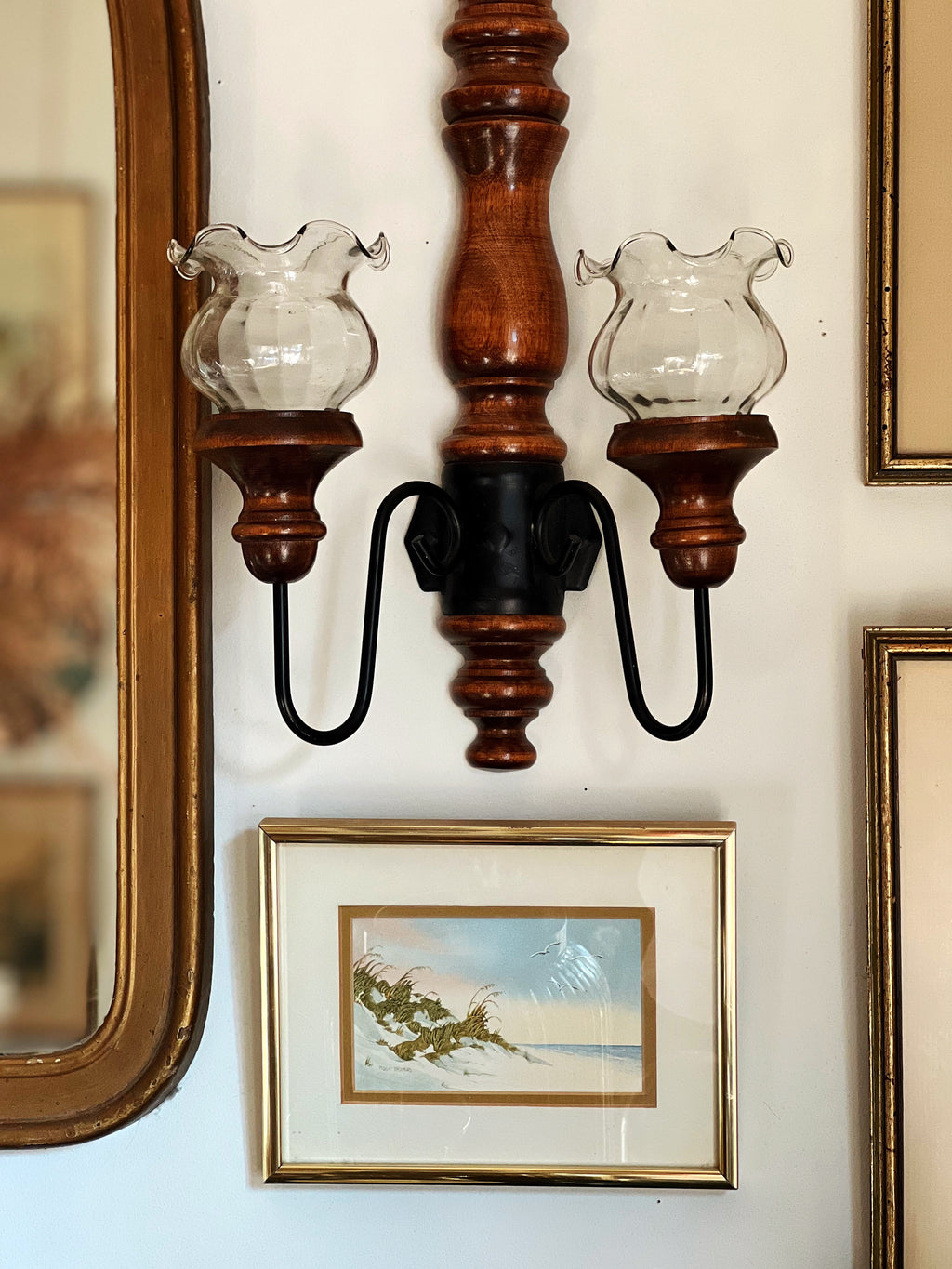 Wooden wall sconce with glass shades on a wall with framed pictures.