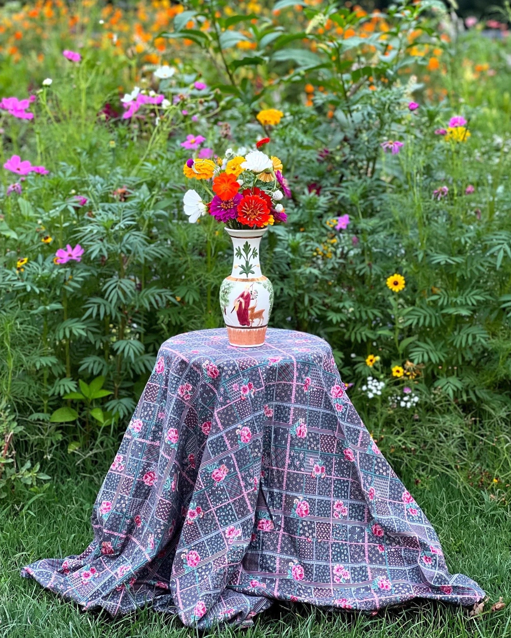 small round table with a floral tablecloth nestled in the middle of a  garden 