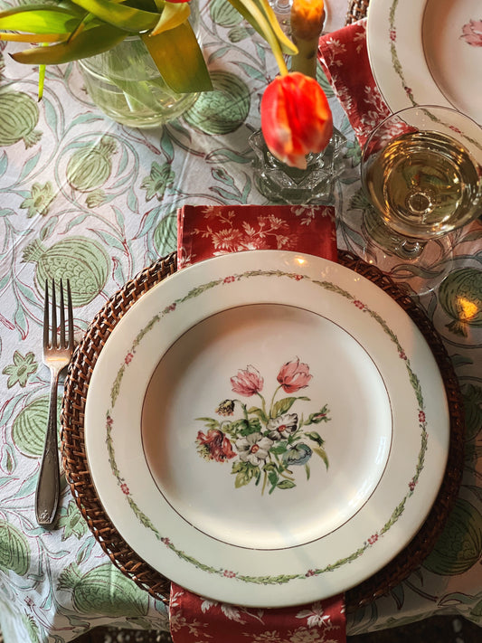 pink and green floral dinner plate on a block print tablecloth with a pink floral napkin and rattan charger