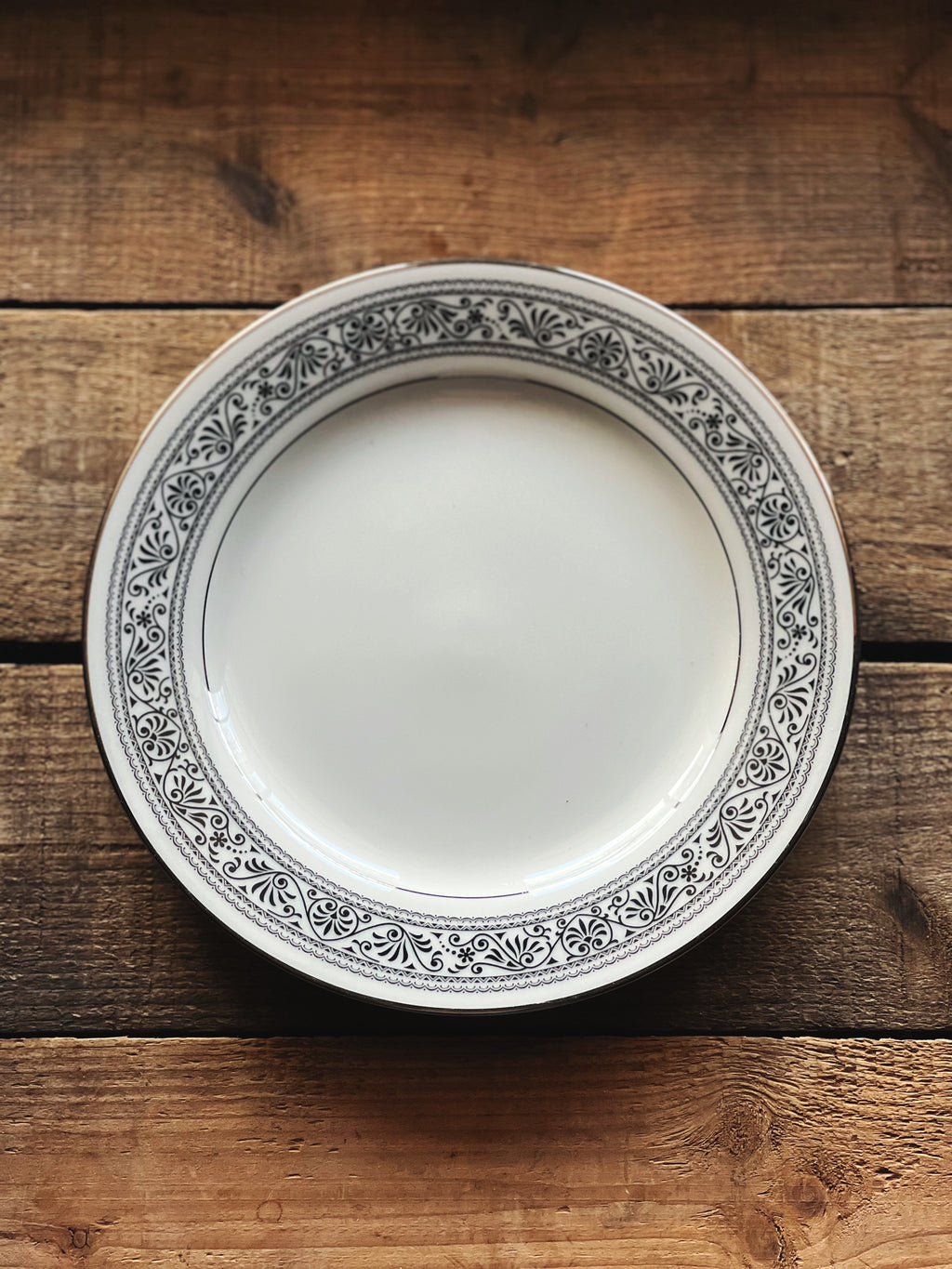black and white salad plate with a scrollwork design and silver rim