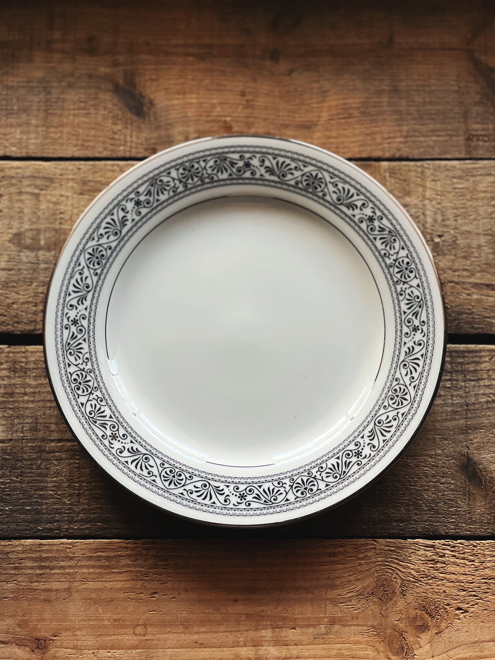 black and white salad plate with a scrollwork design and silver rim