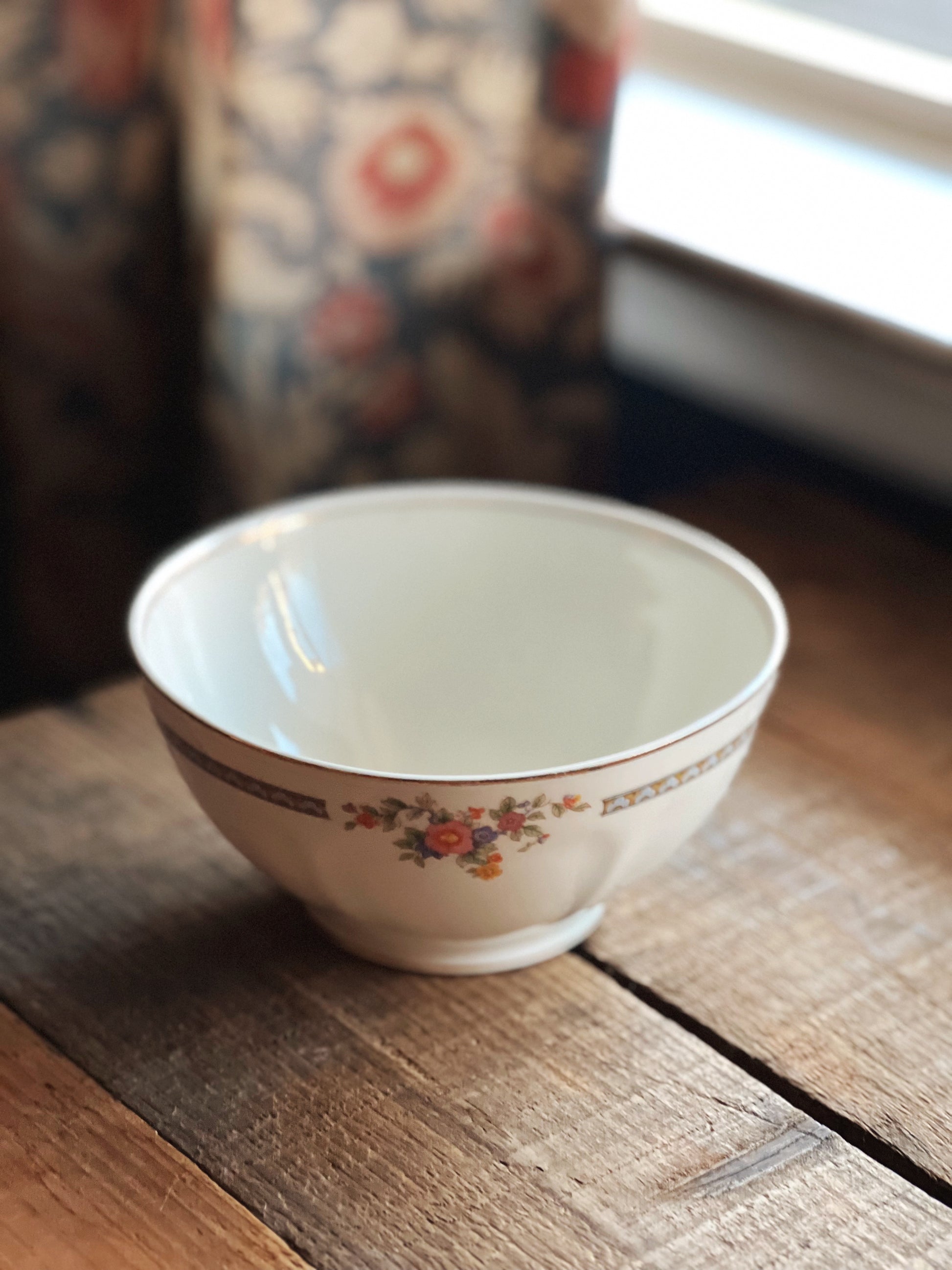 Decorative ceramic bowl on a wooden surface with a blurred floral-patterned curtain in the background.