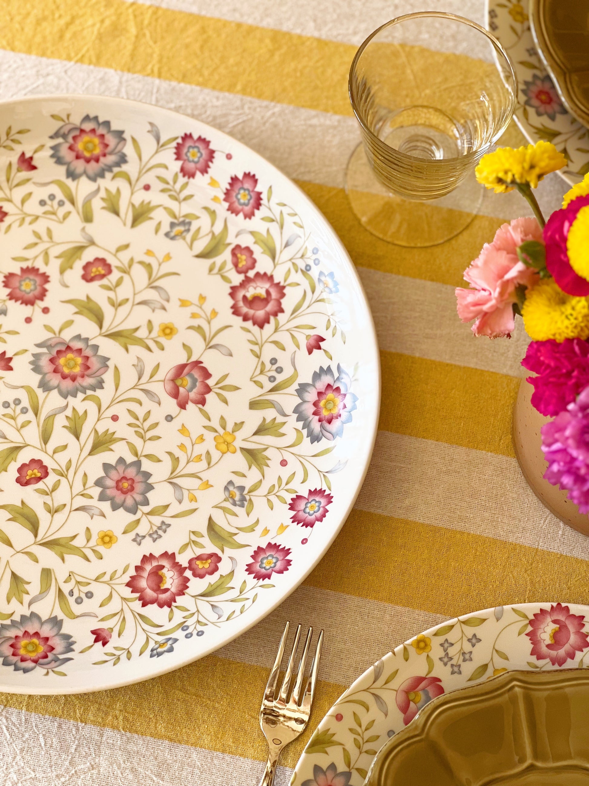 multi color floral platter on a table set with a yellow stripe tablecloth