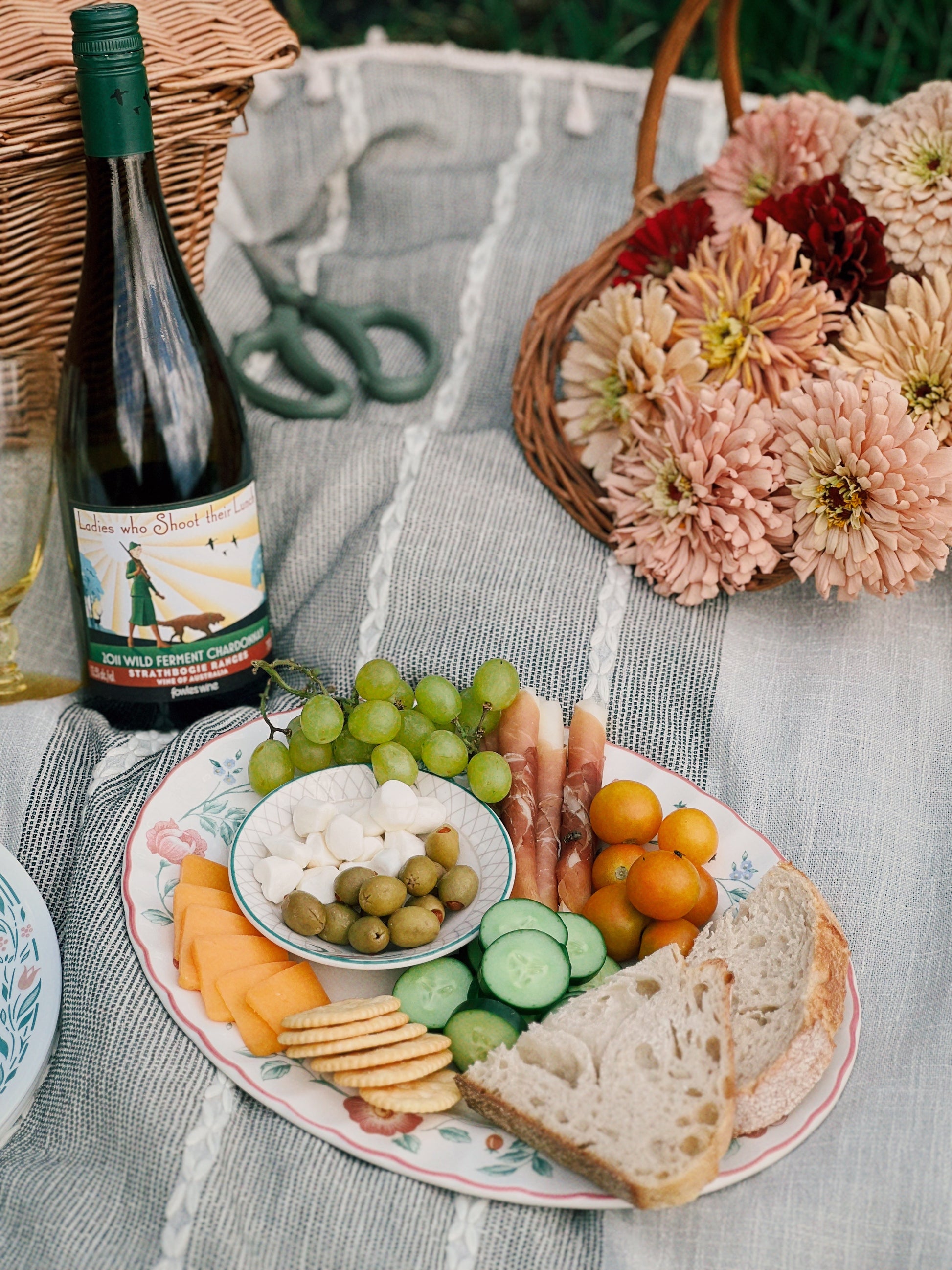 Wine bottle, platter of snacks, and flowers on a picnic blanket