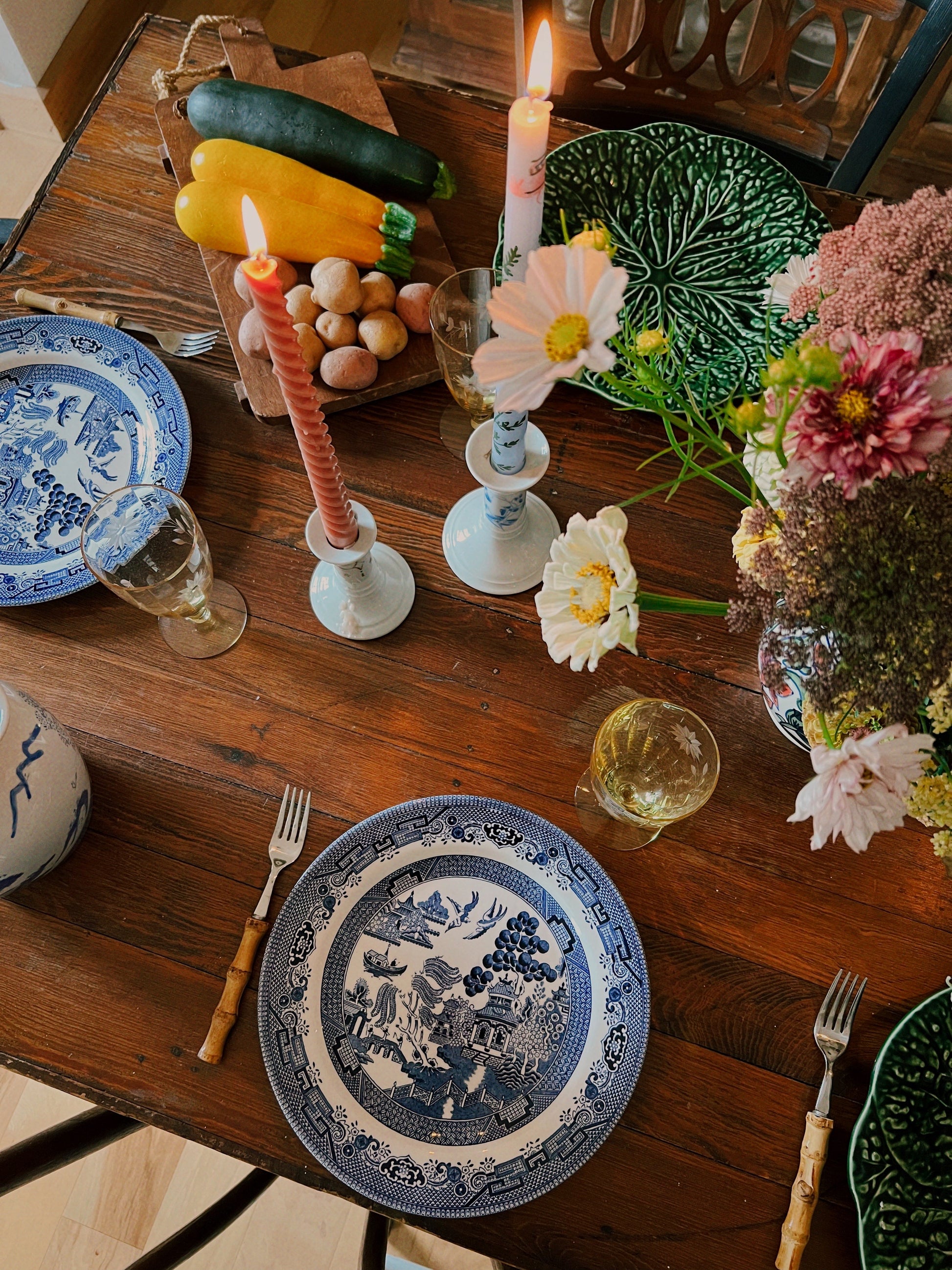 Decorative table setting with plates, candles, and flowers on a wooden table.