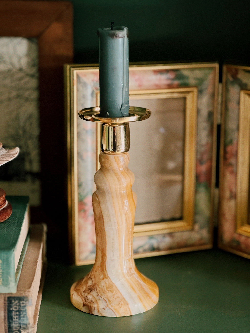Candle in a marble-patterned candlestick holder with books and a mirror in the background