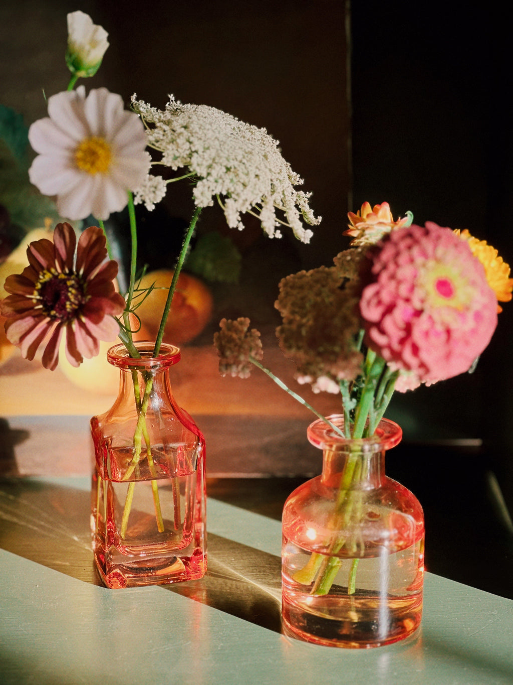 Two small pink vases with flowers on a reflective surface