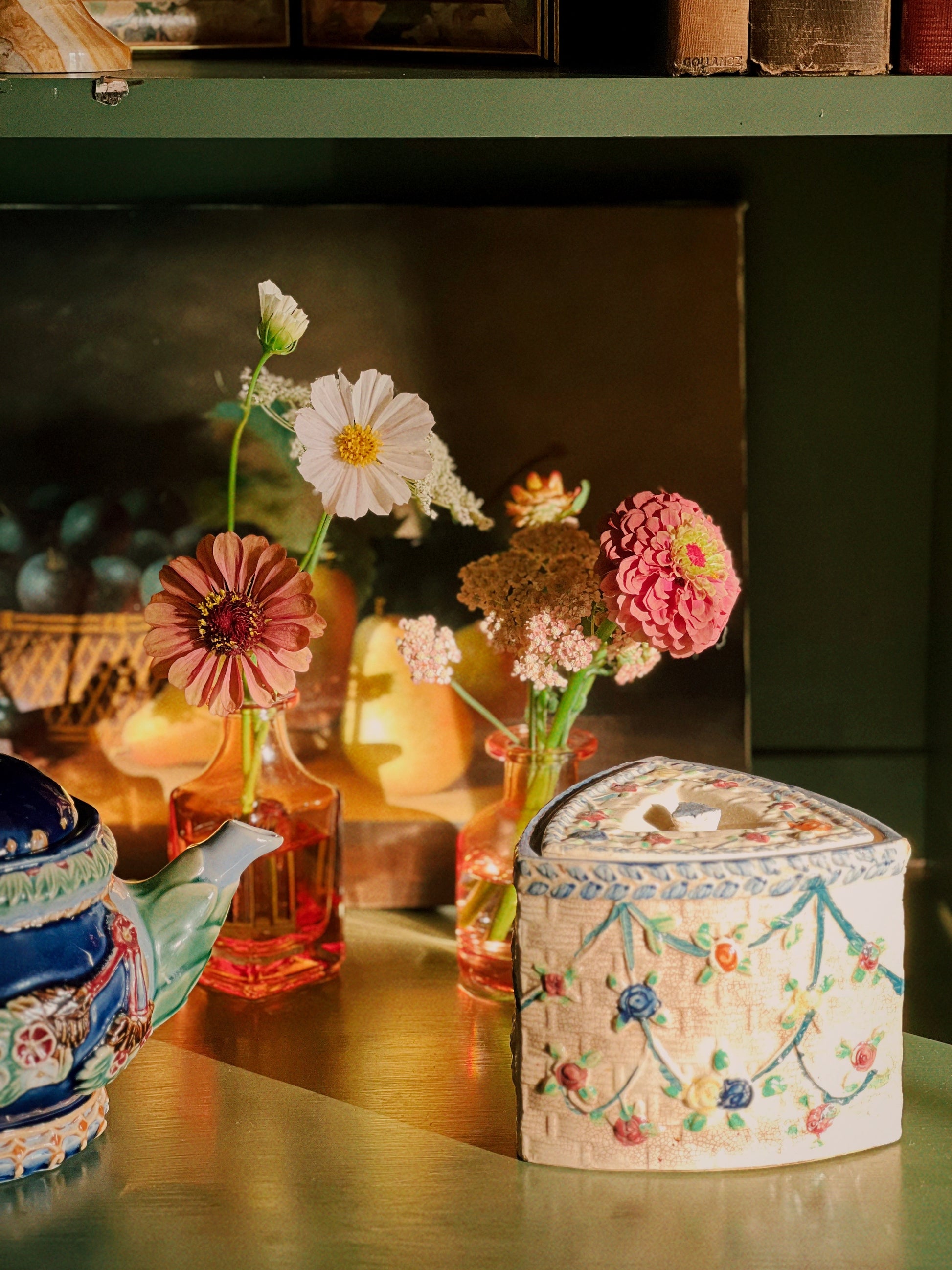 Decorative teapot, flowers, and embroidered box on a wooden surface with a blurred background.