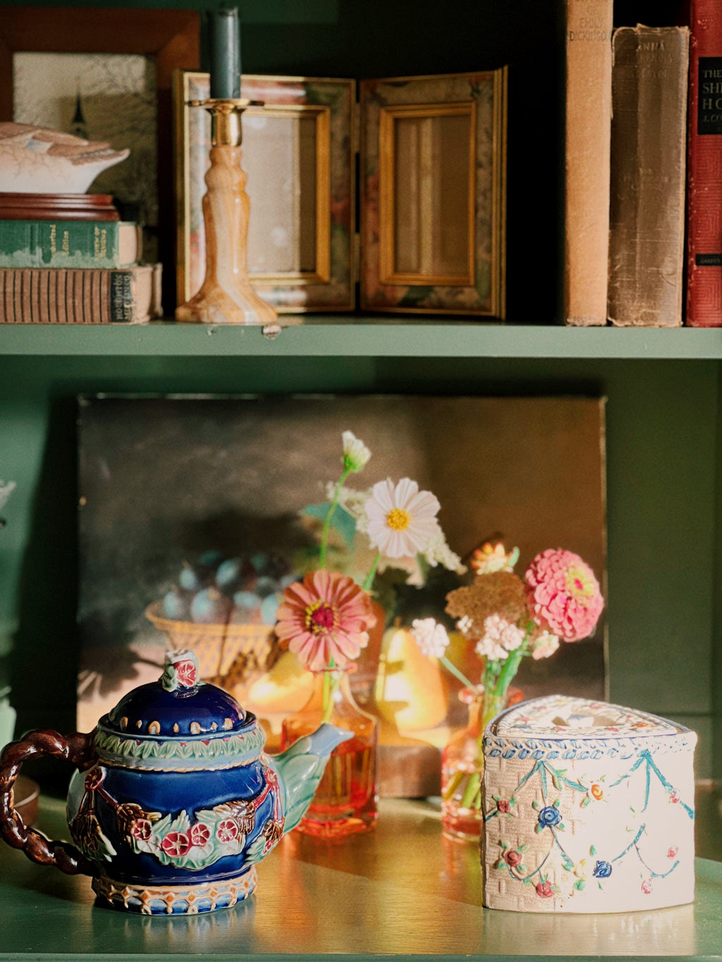 Decorative shelf with a teapot, flowers, and books in a cozy setting.