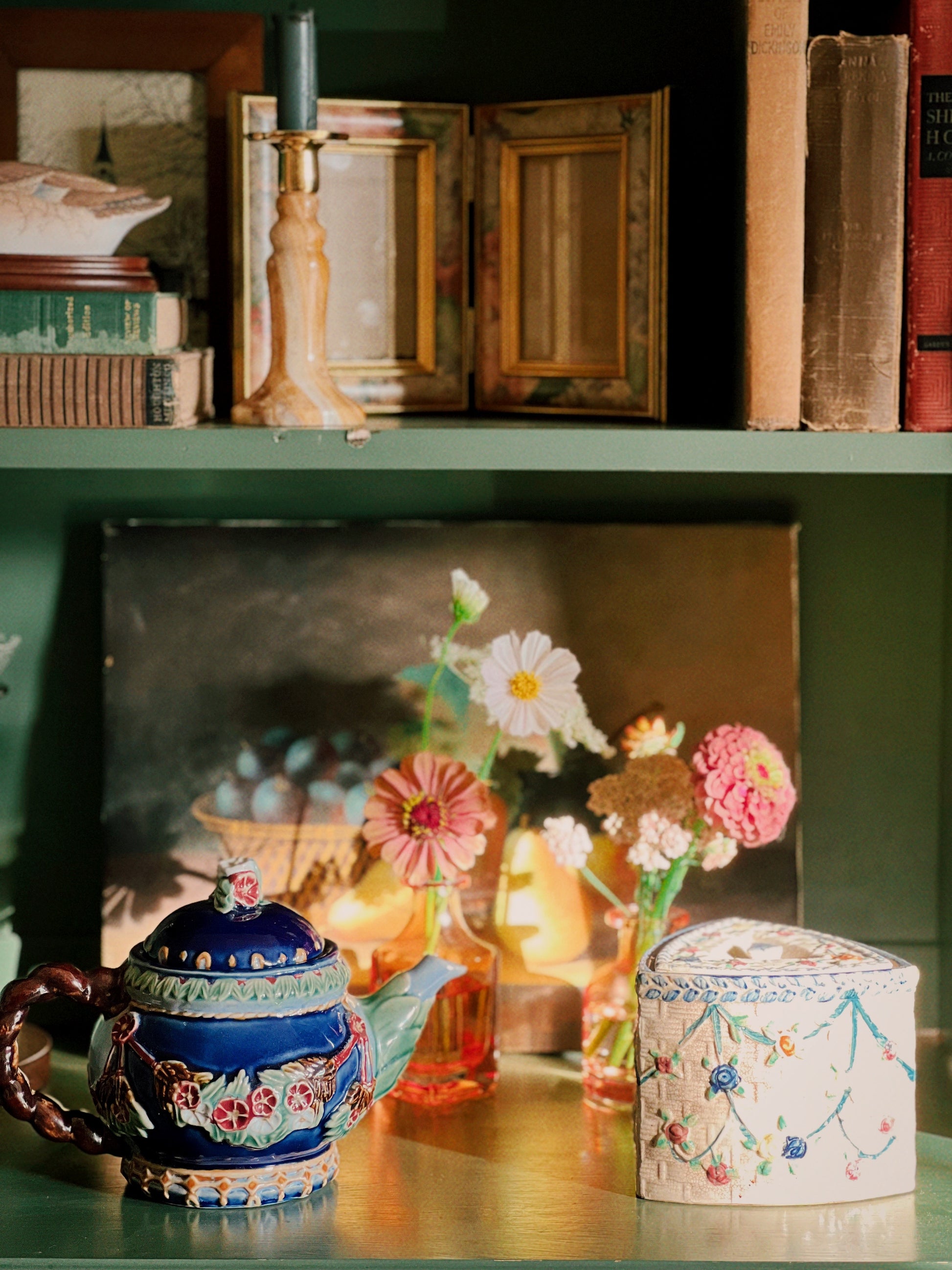 Decorative shelf with a teapot, flowers, and books in a cozy setting.