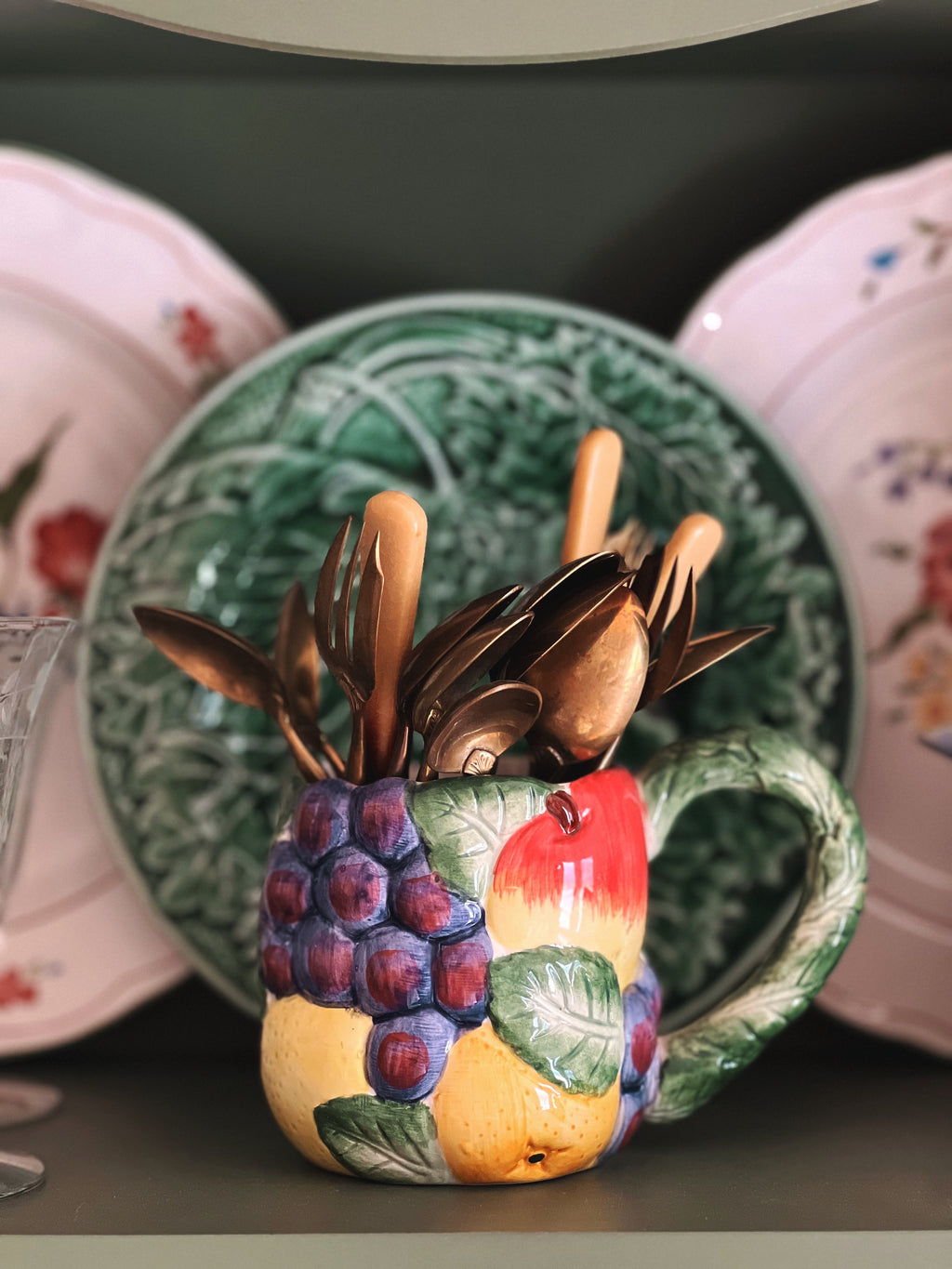 Decorative fruit-themed spoon holder with cutlery on a table with plates in the background