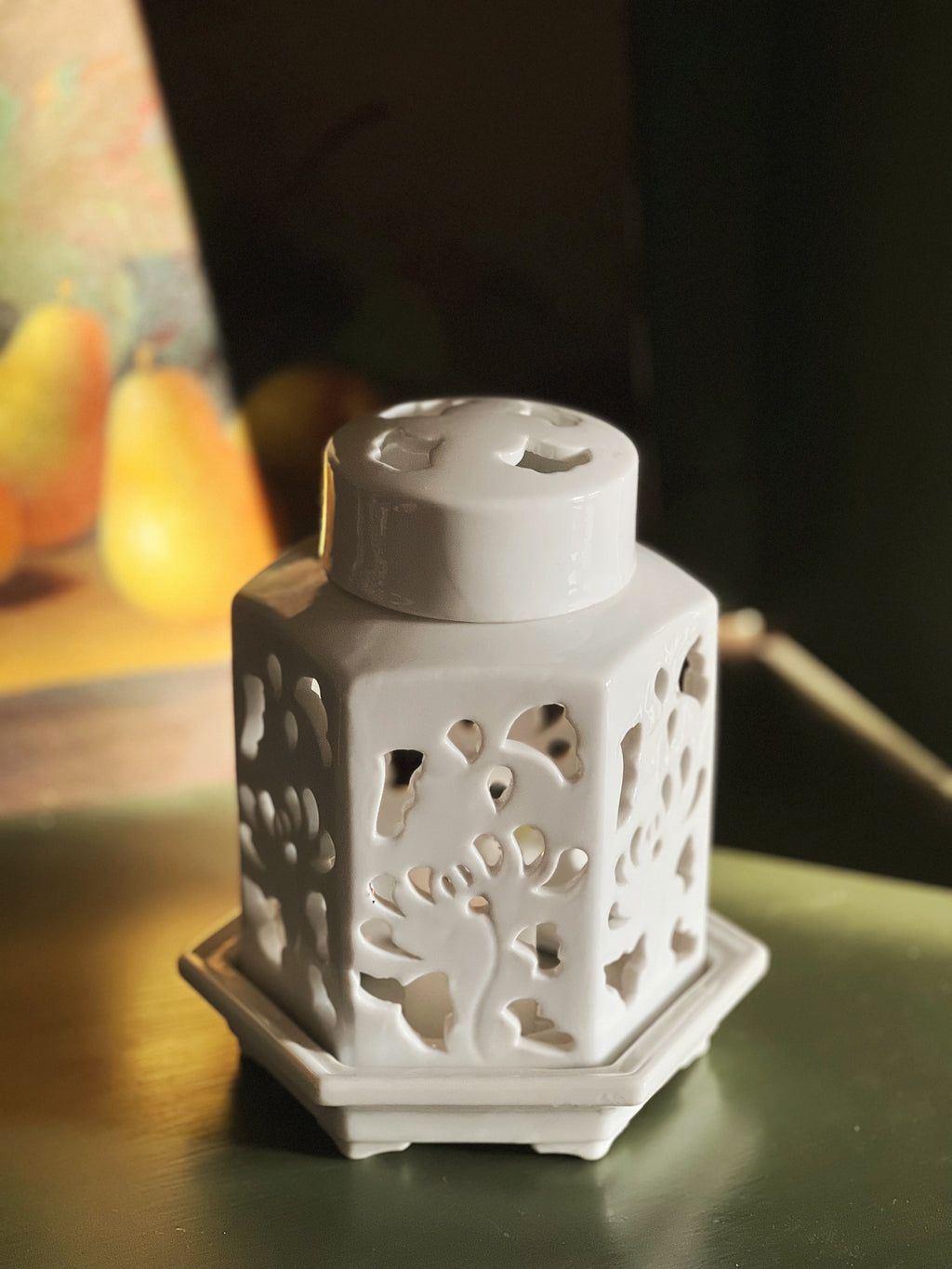 Decorative white ceramic lantern with intricate cut-out patterns on a dark surface.