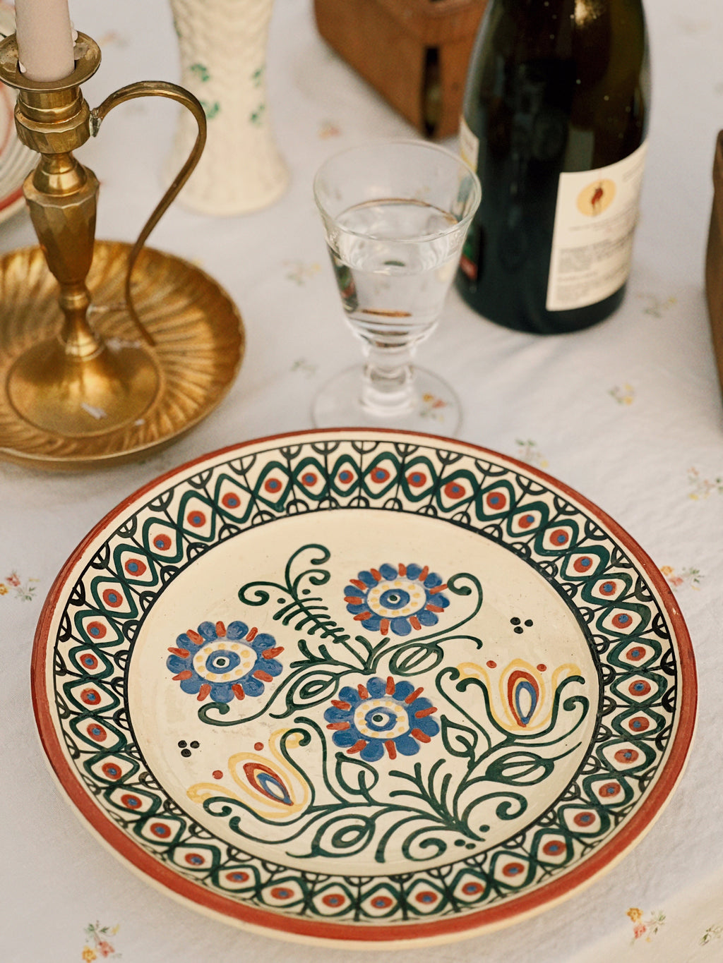 Decorative ceramic plate with floral patterns on a table with a bottle and glass.