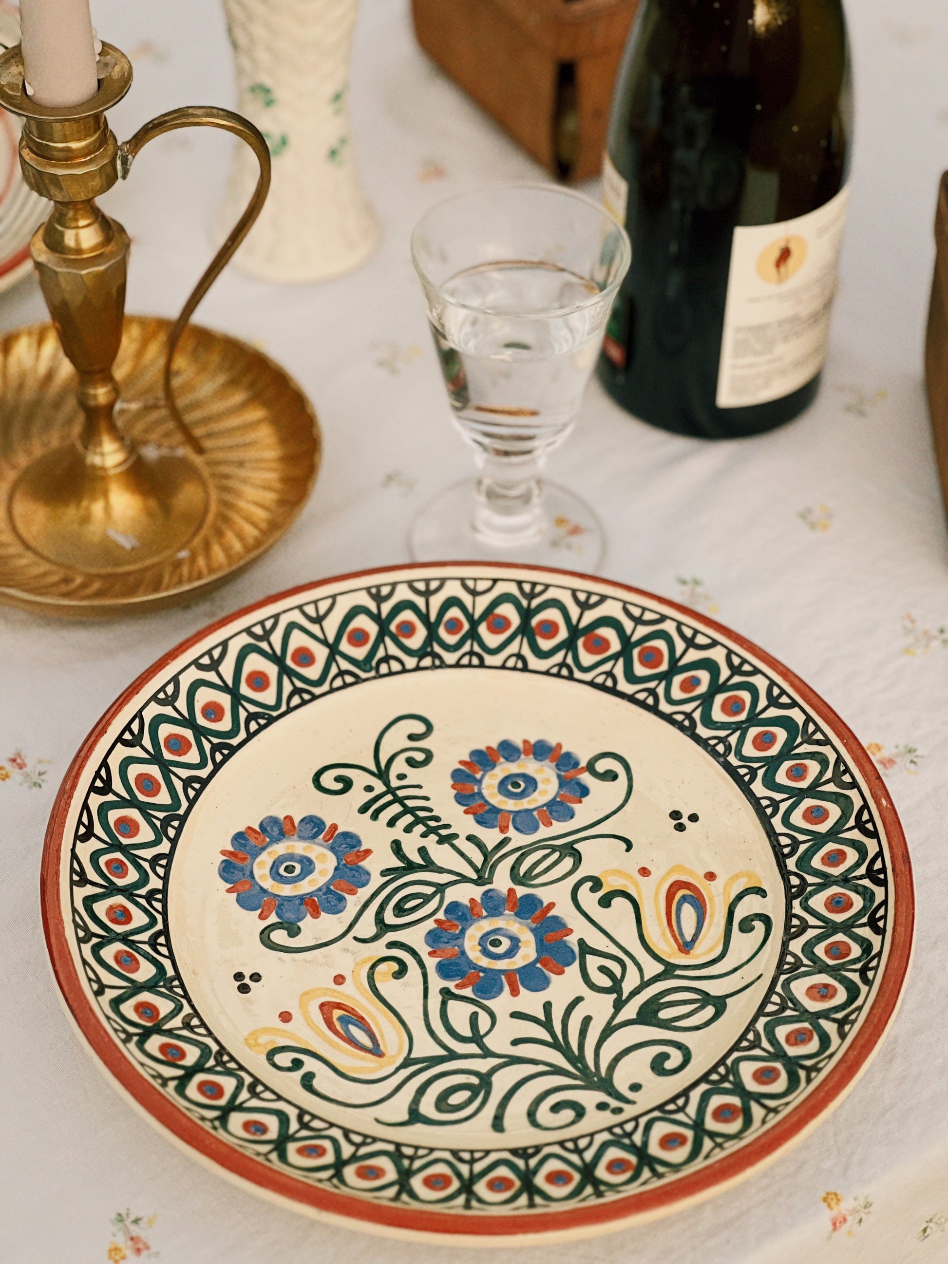 Decorative ceramic plate with floral patterns on a table with a bottle and glass.
