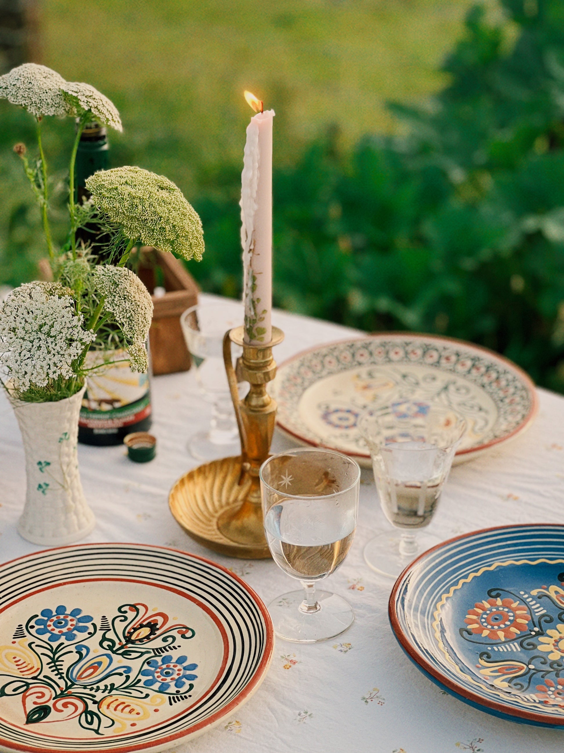 Decorative table setting with ceramic plates, glasses, and a candle outdoors.