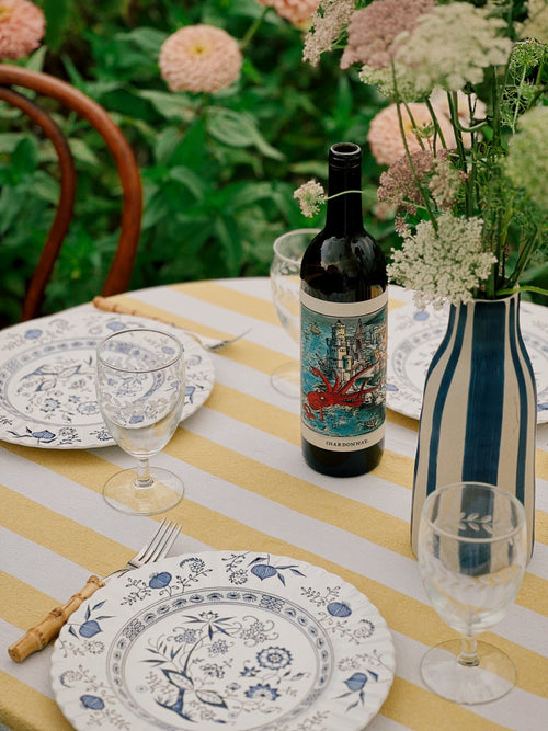 Set table with wine bottle, glasses, and floral arrangement on a striped tablecloth.