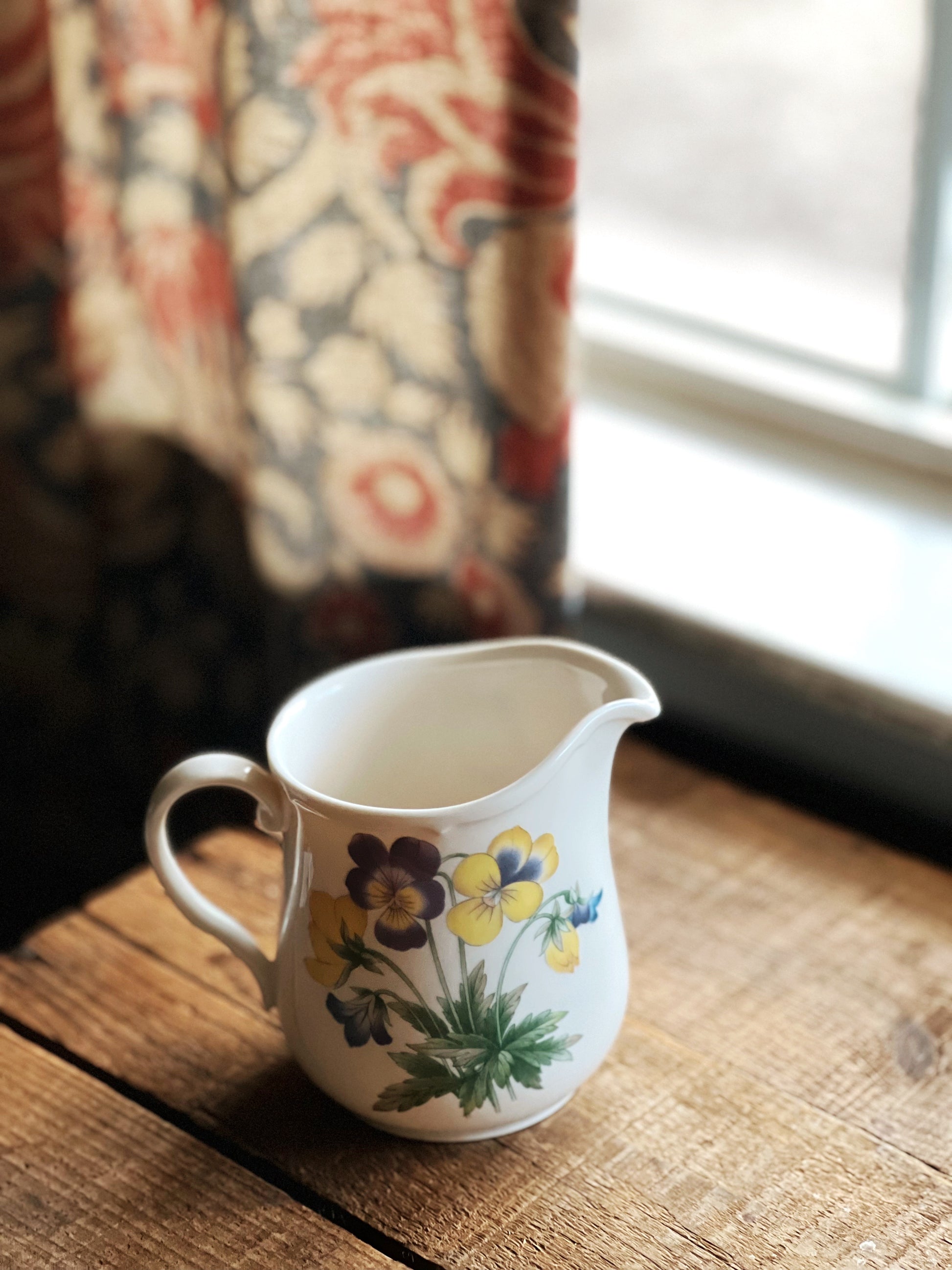 Decorative ceramic pitcher with floral design on a wooden surface