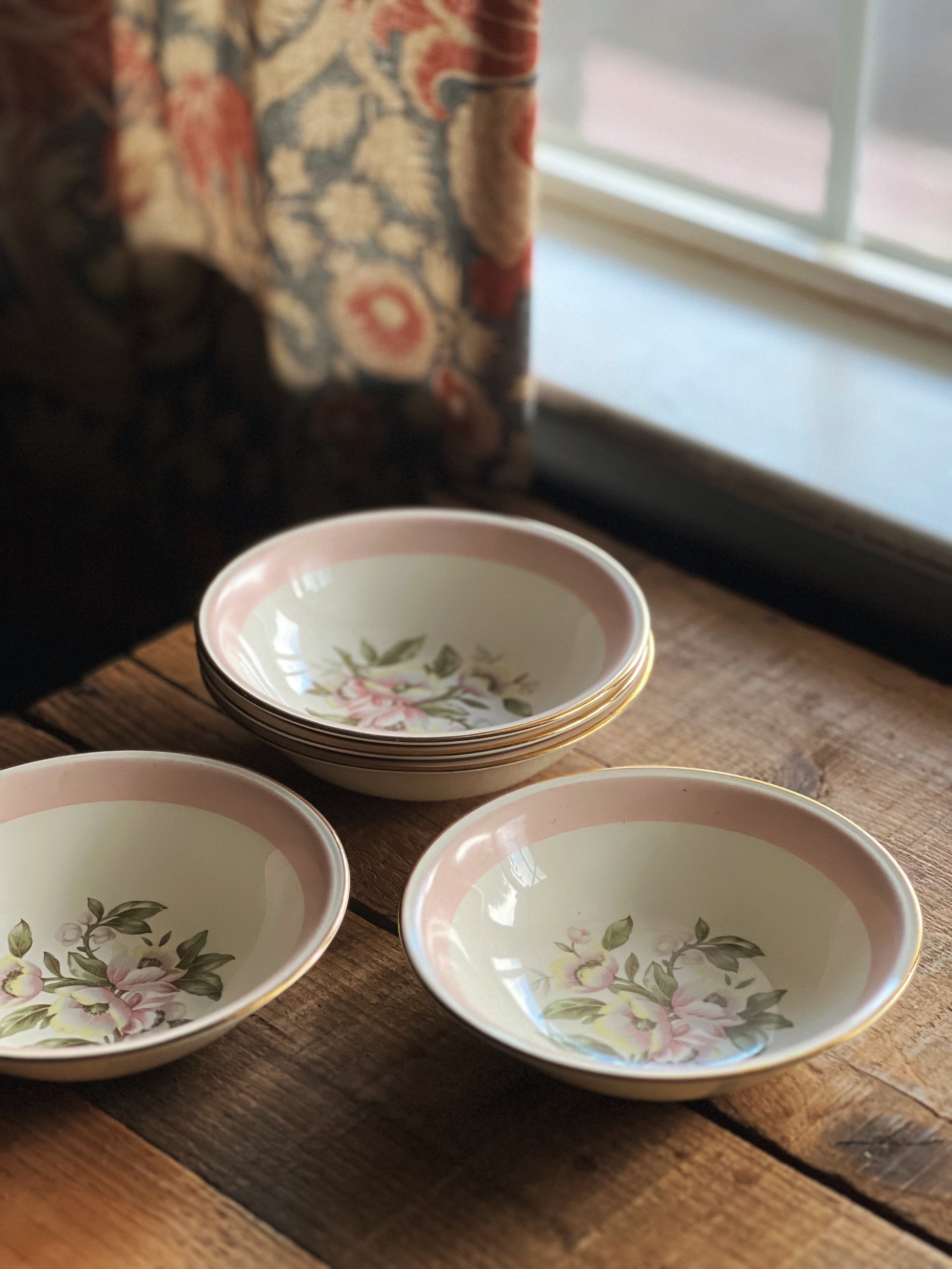 Set of ceramic bowls with floral patterns on a wooden surface near a window.