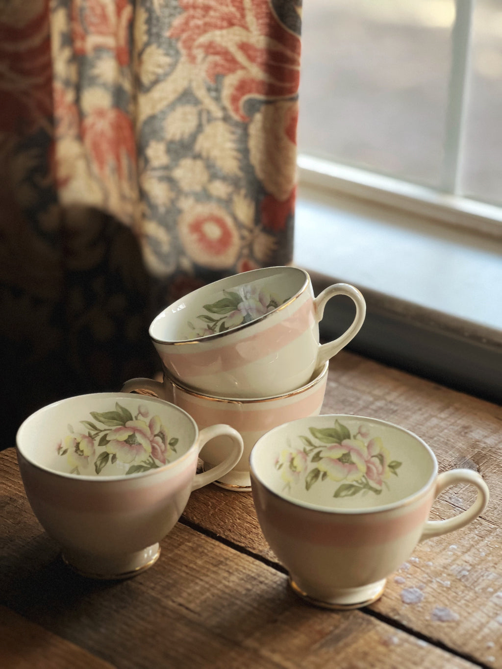 Overhead view of a set of floral teacups on a wooden surface with a window in the background