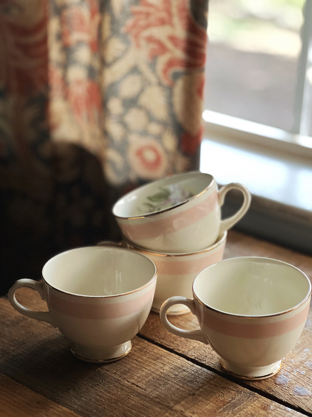 Three Homer Laughlin teacups on a wooden surface with a patterned curtain in the background.
