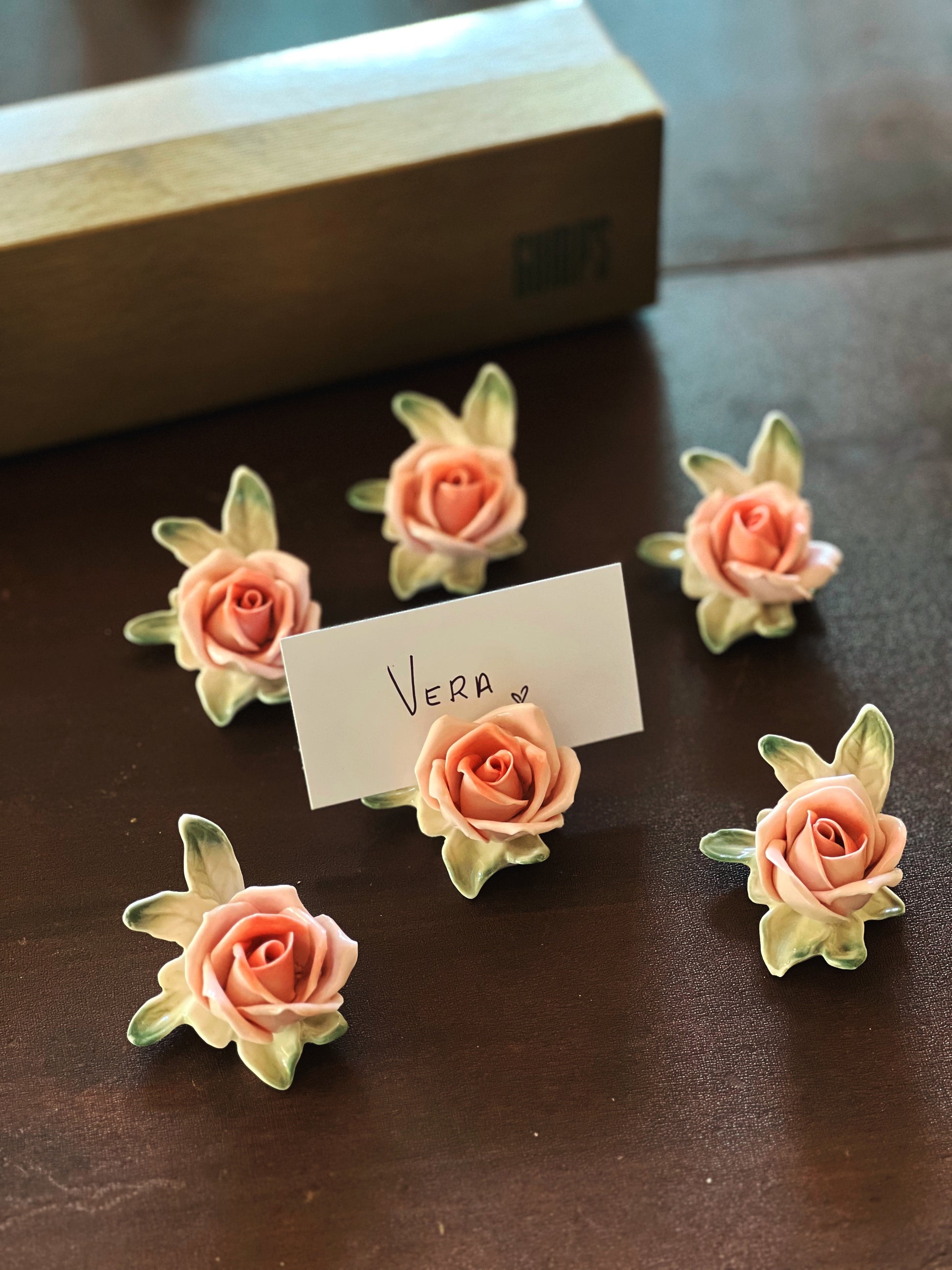 Set of decorative rose-shaped items with a card labeled 'Vera' on a dark surface.