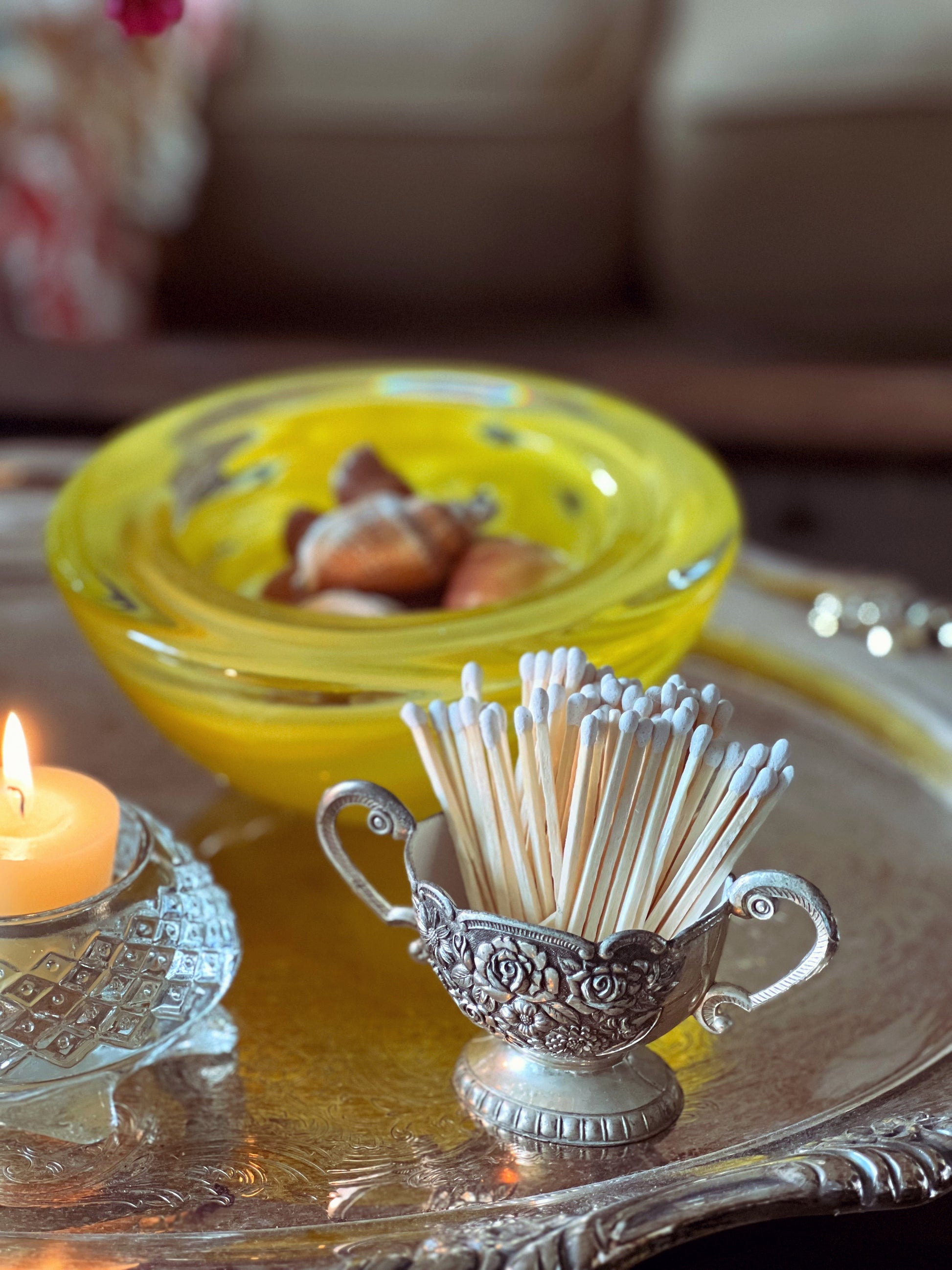 Decorative matchstick holder with matches on a table with a candle and shell dish in the background.