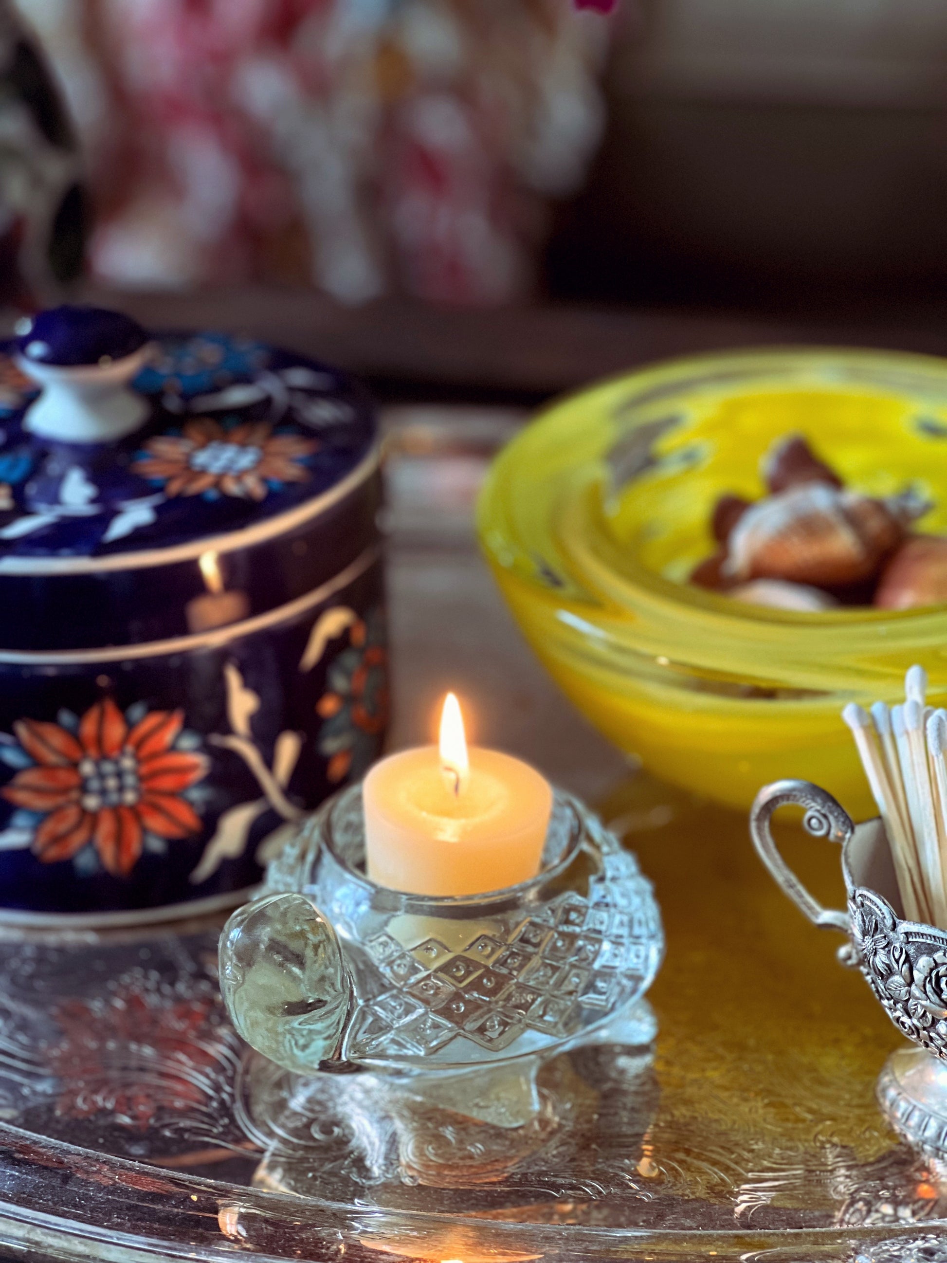 Candle in a decorative holder with colorful containers and a blurred background