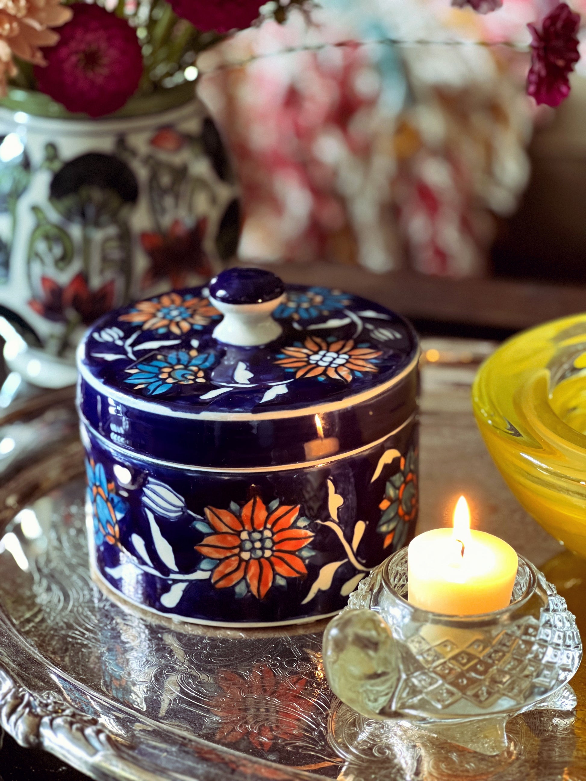 Decorative blue container with floral patterns on a reflective surface with a lit candle.