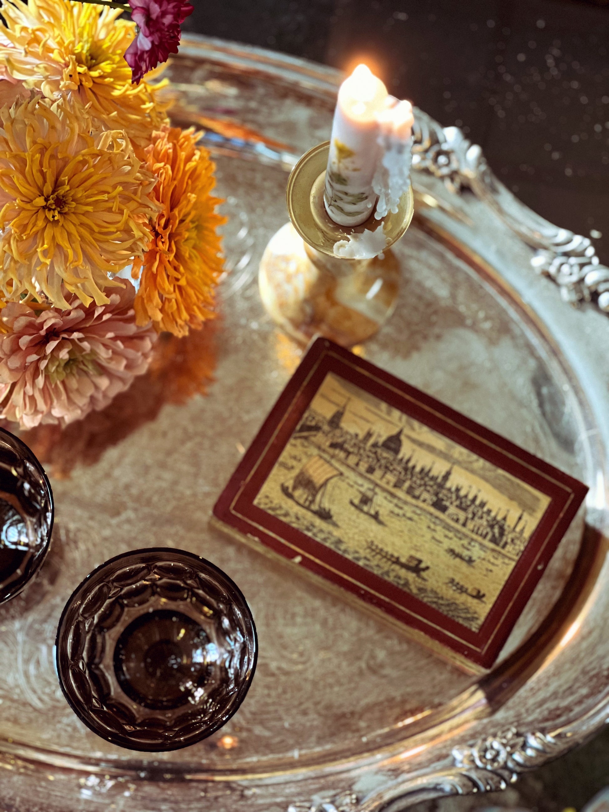 Decorative tray with flowers, candle, and vintage card on a reflective surface