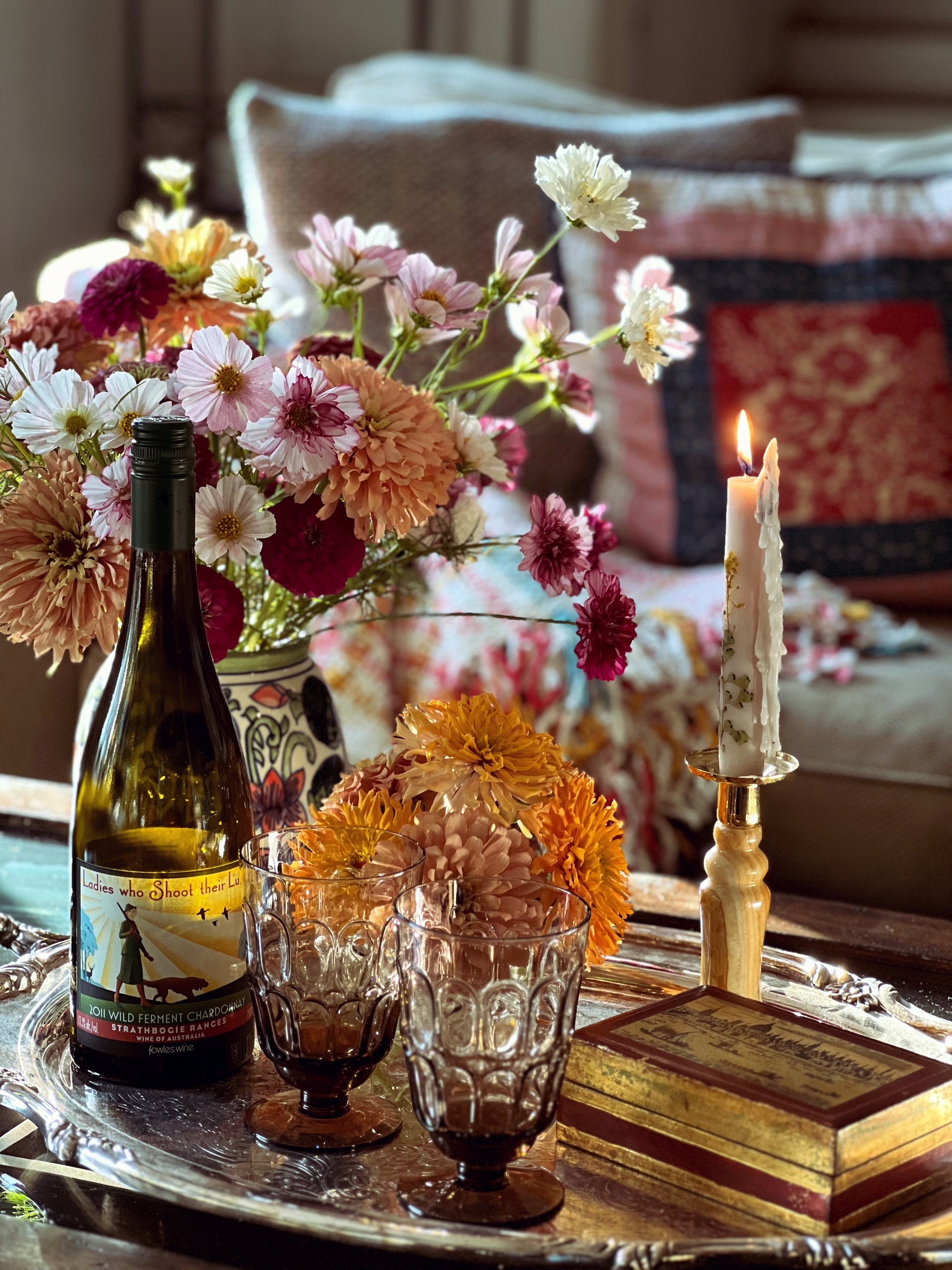 Wine bottle, glasses, and flowers on a table with a candle and decorative items.