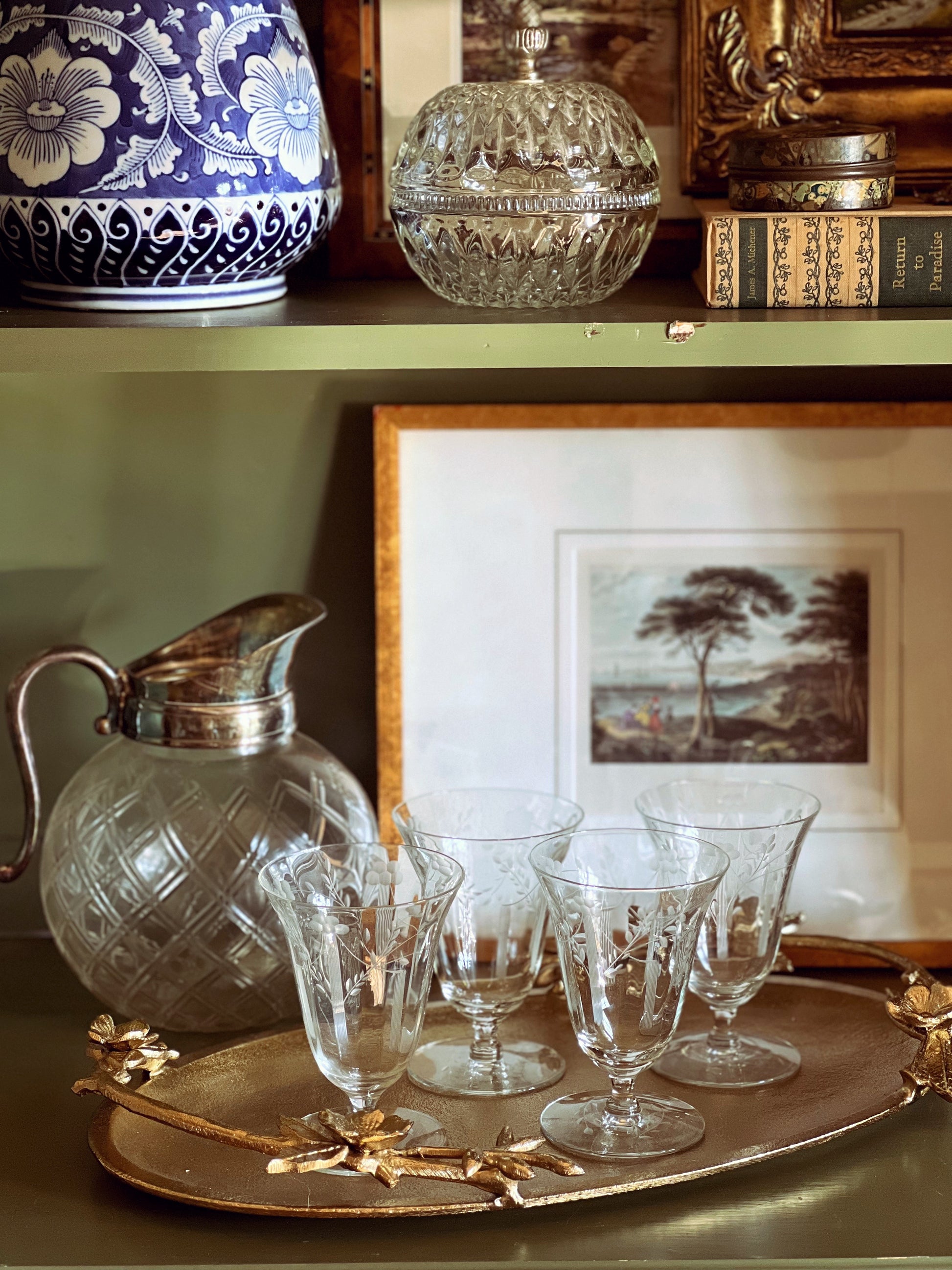 Decorative glassware and pitcher on a tray with a framed picture in the background