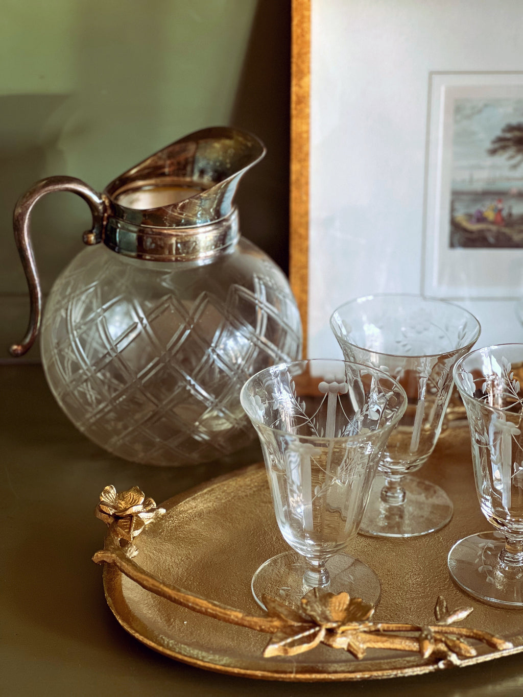 Clear glass pitcher and glasses on a gold tray with a decorative handle.