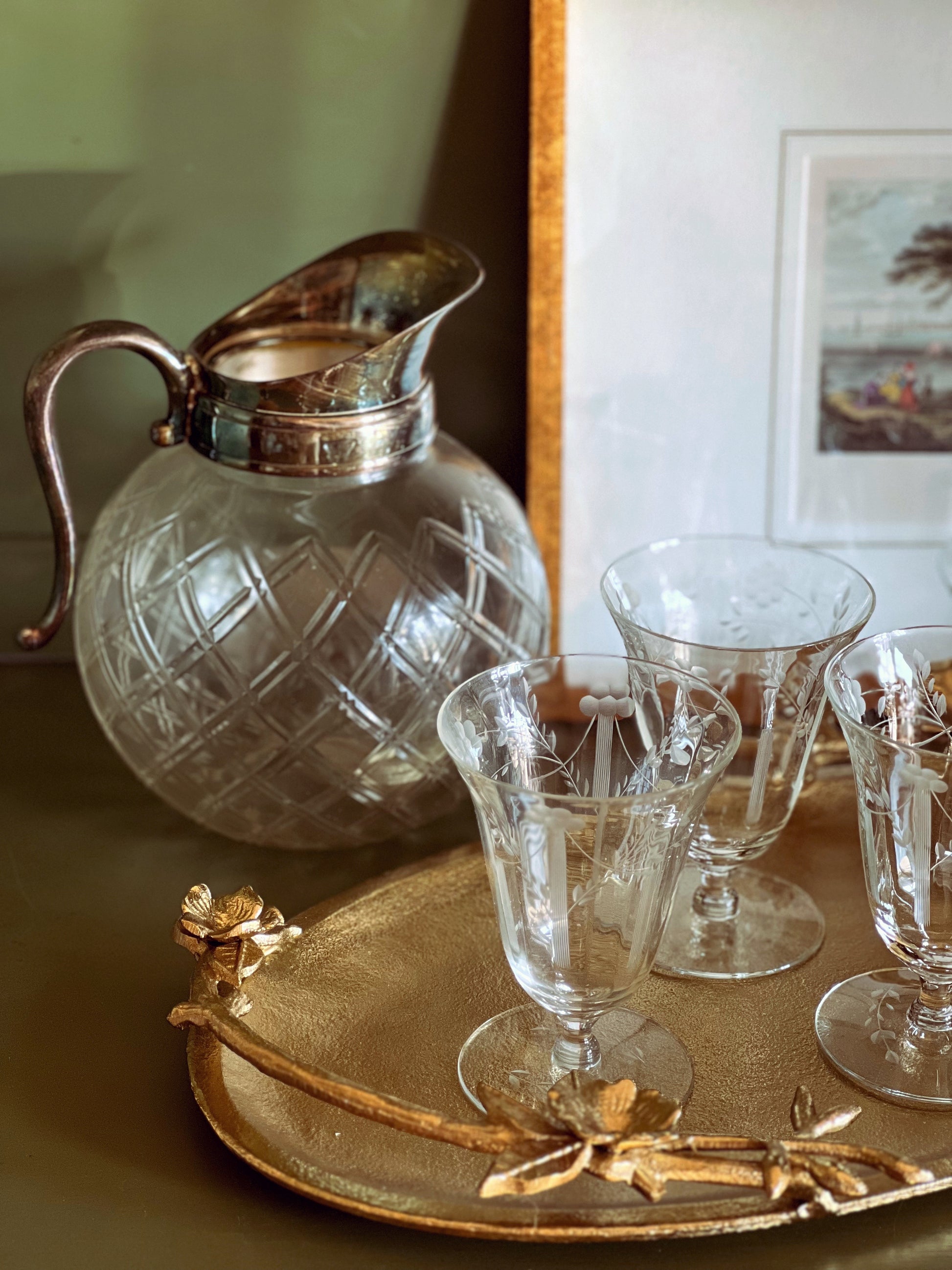 Clear glass pitcher and glasses on a gold tray with a decorative handle.
