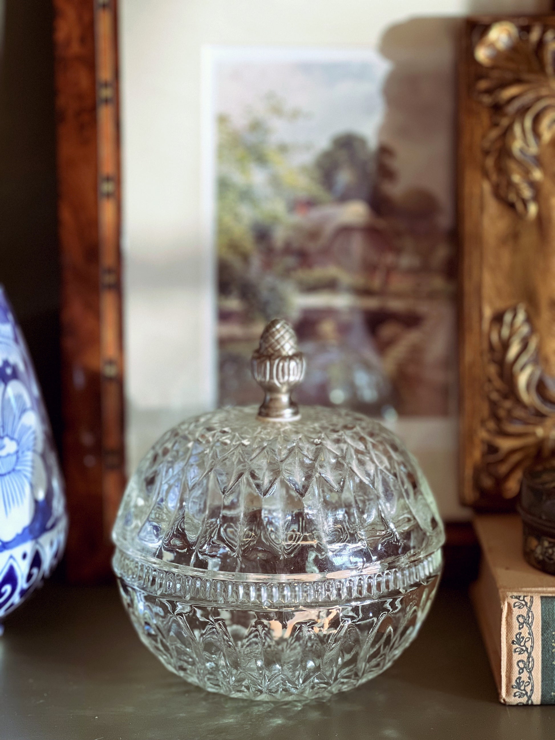 Decorative glass container with a silver lid on a surface with a blurred background