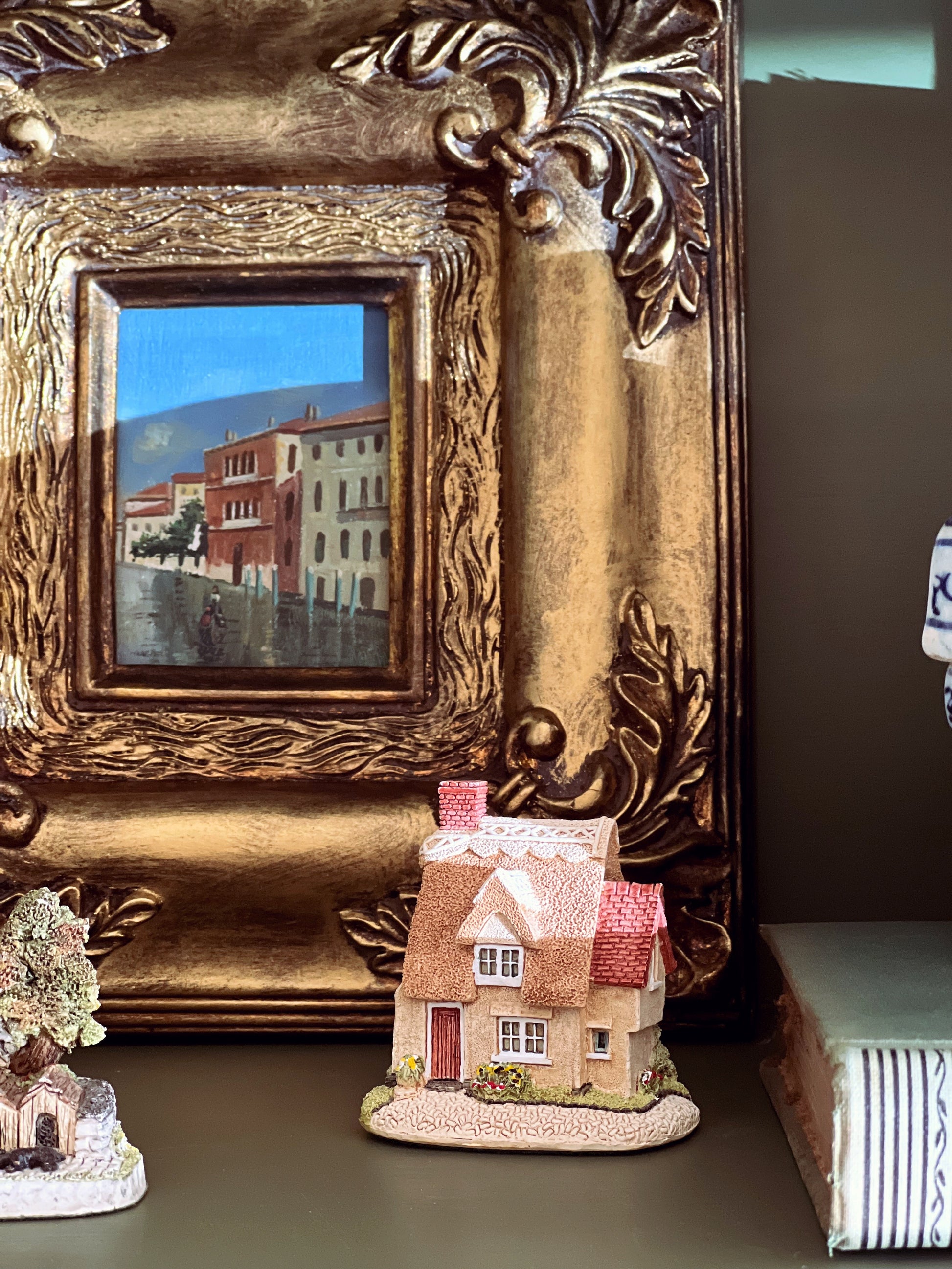 Decorative miniature house with a gold ornate frame in the background