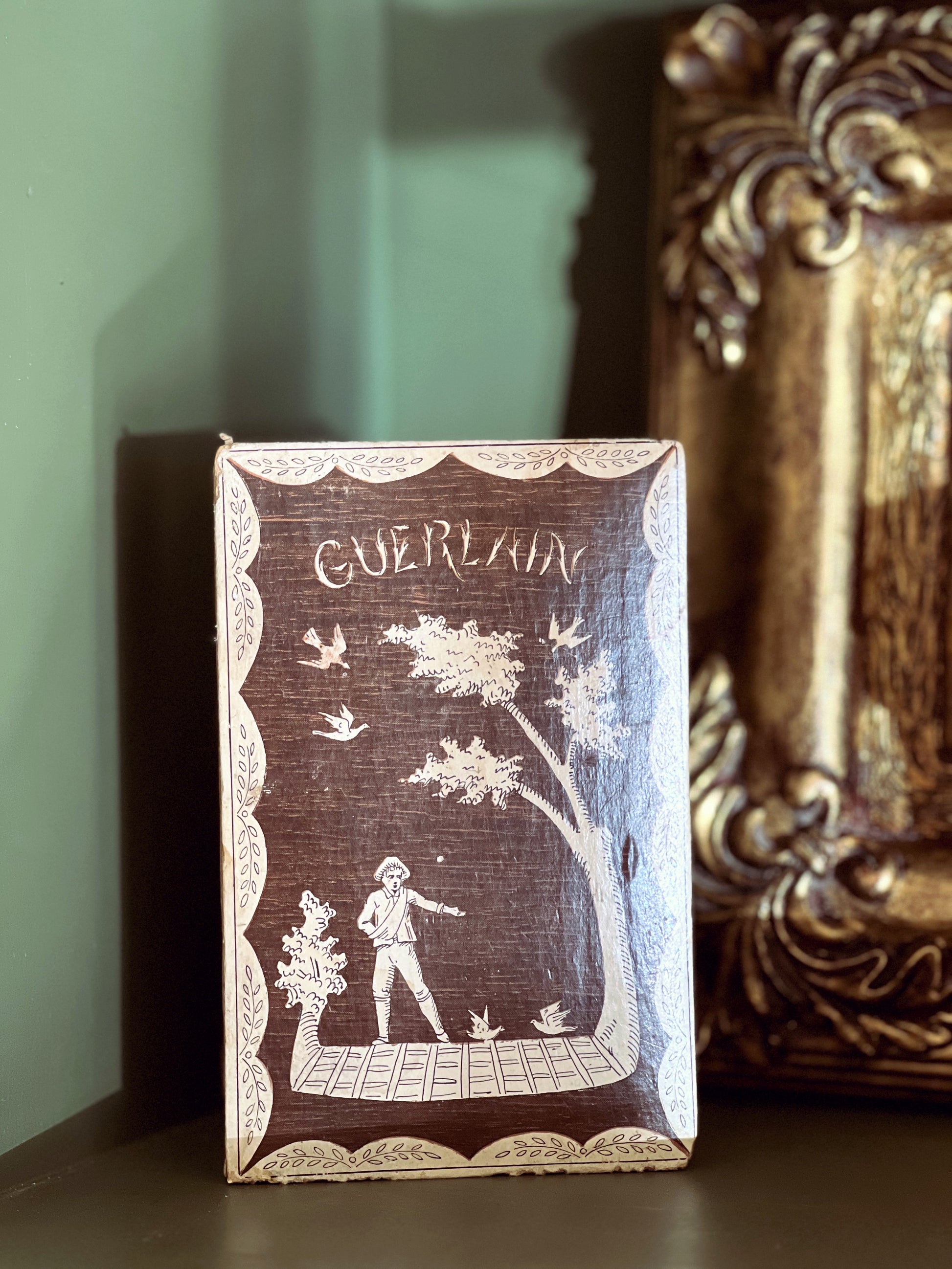 Decorative box with intricate design and 'Guerlain' branding on a shelf.