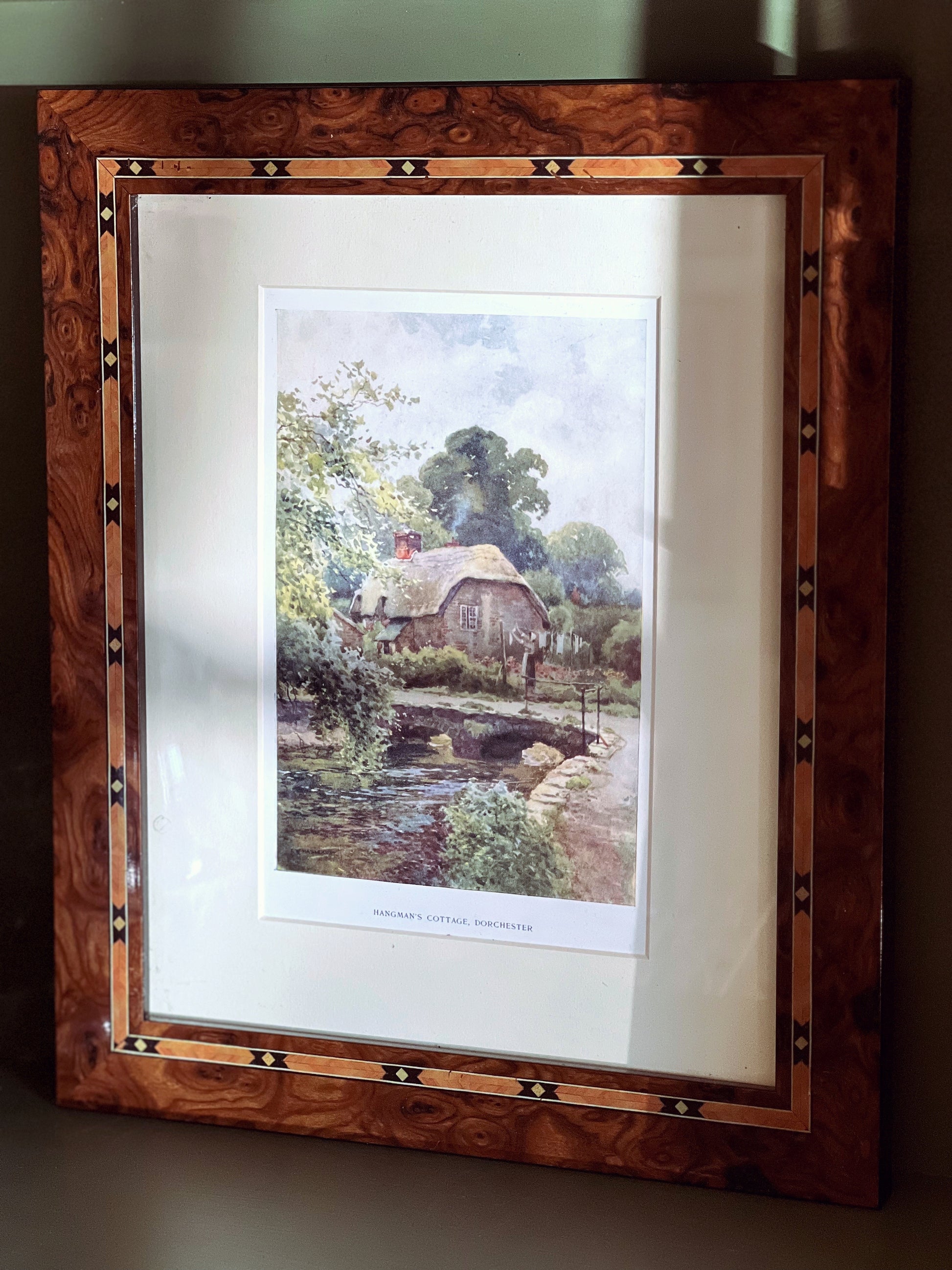 Framed artwork of a landscape with a house and bridge.