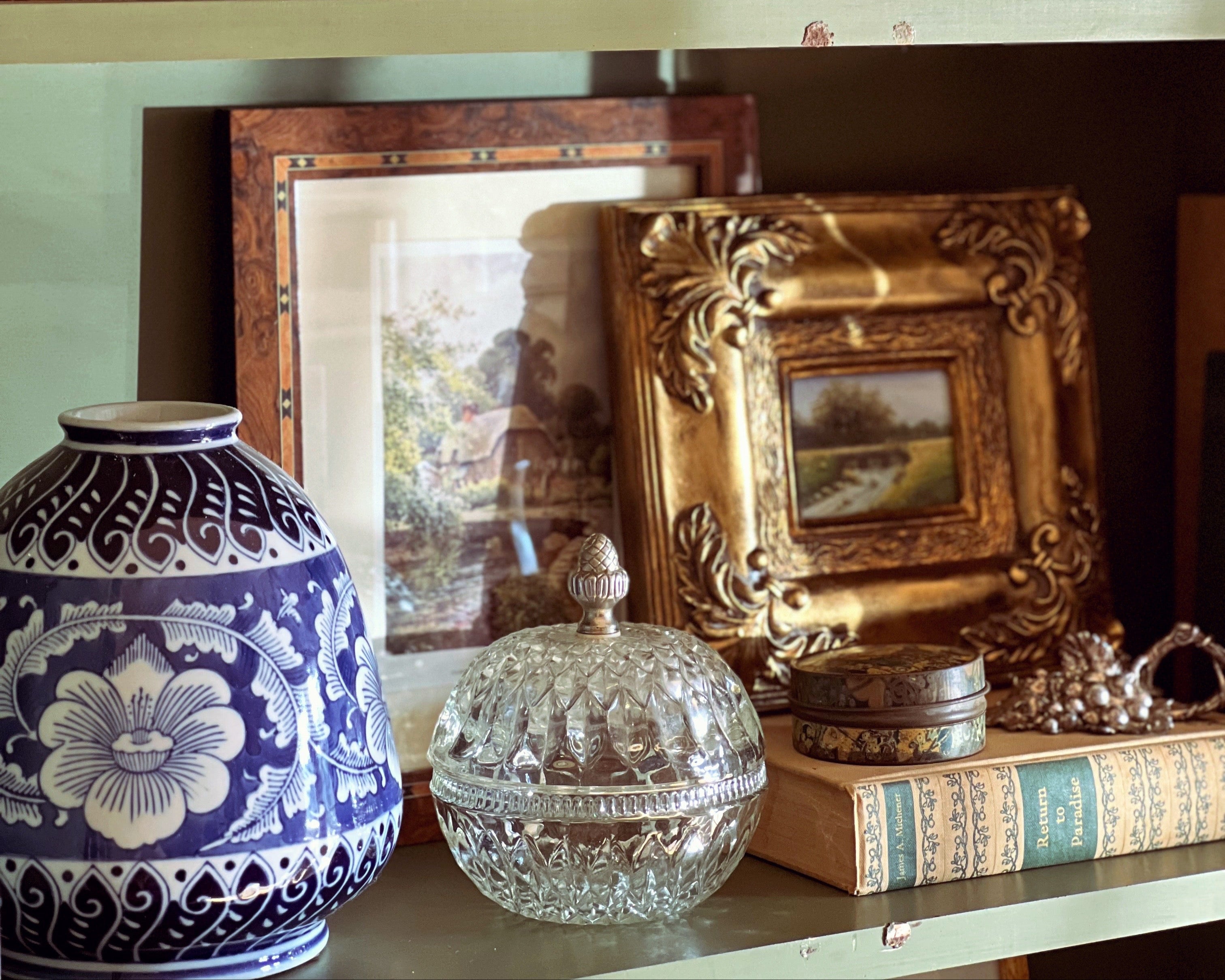 Decorative shelf with antique frames, vases, and books against a dark wall.