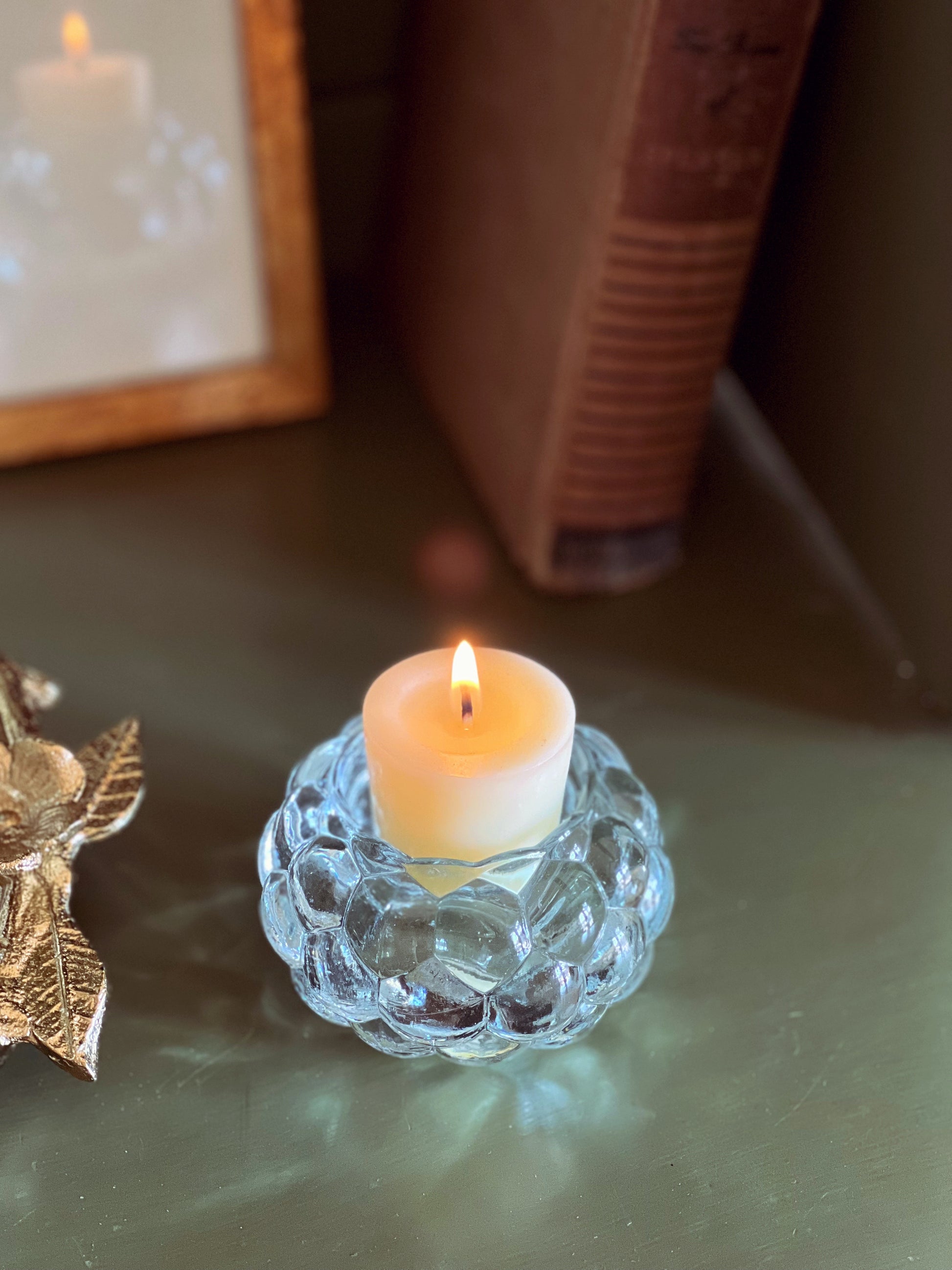 Candle in a decorative glass holder on a reflective surface with a blurred background