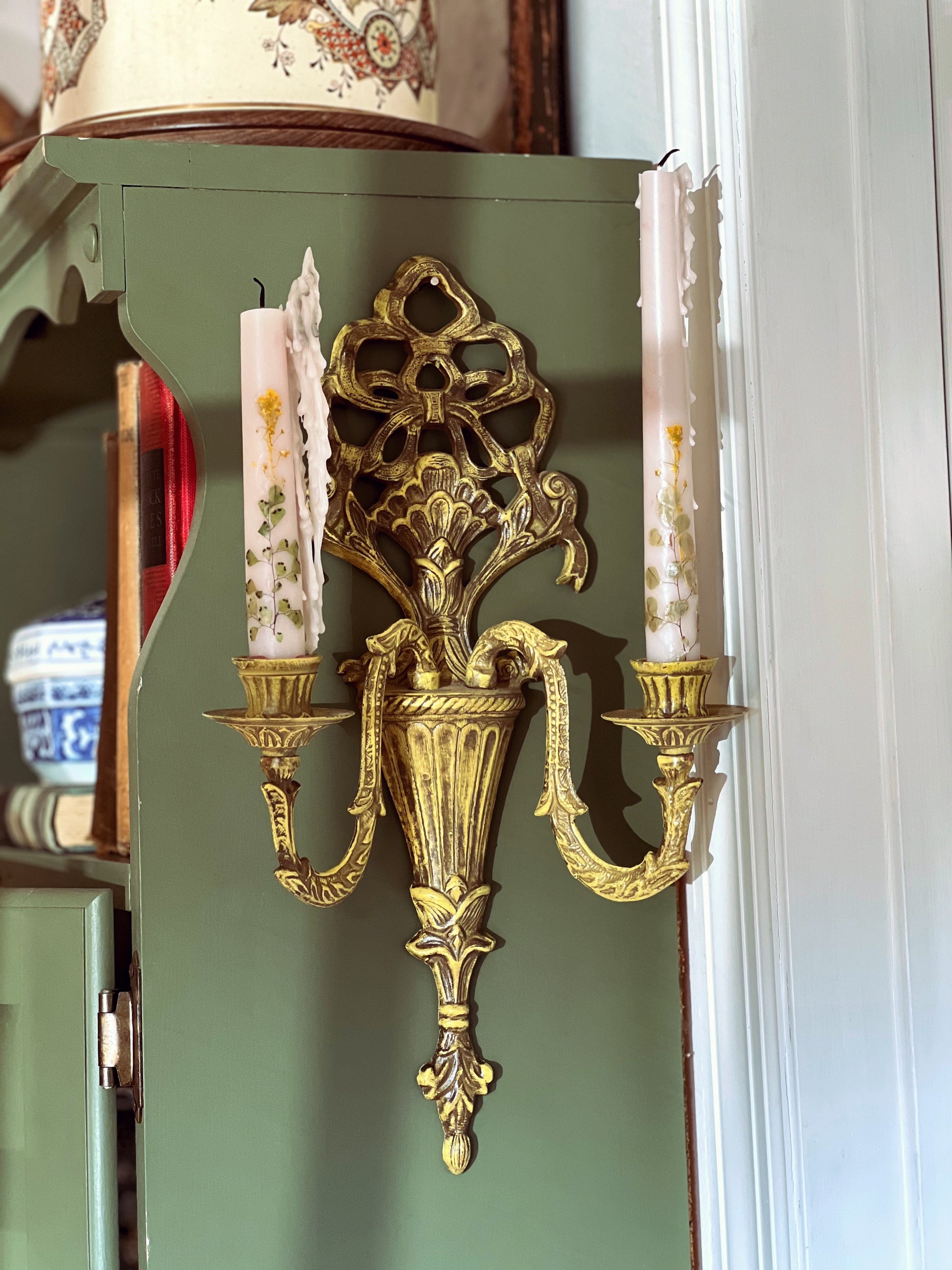 Decorative gold wall sconce with candles on a green wall.